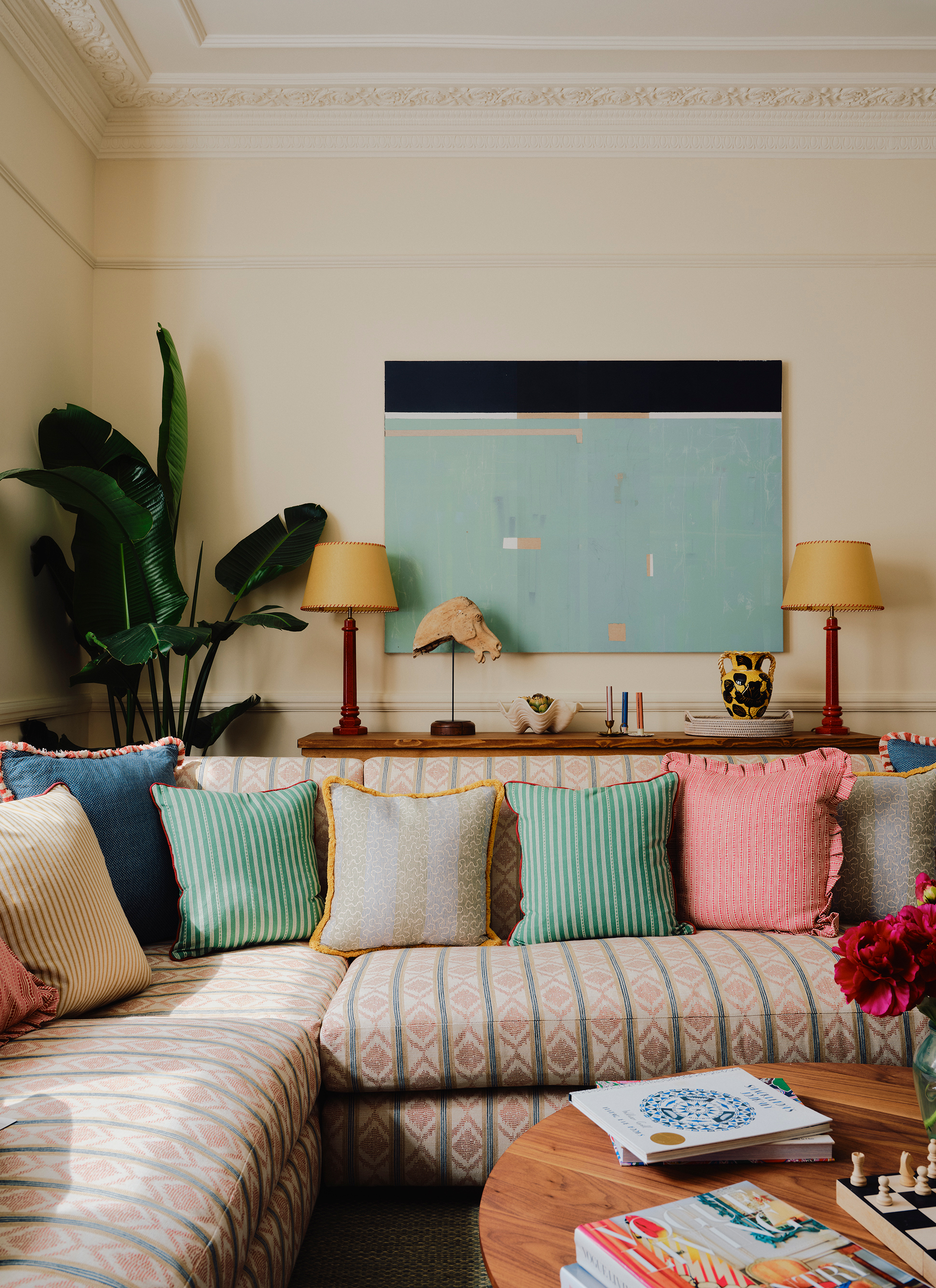a living room with a cream, green stripe and red patterned l shape sofa filled with colourful cushions