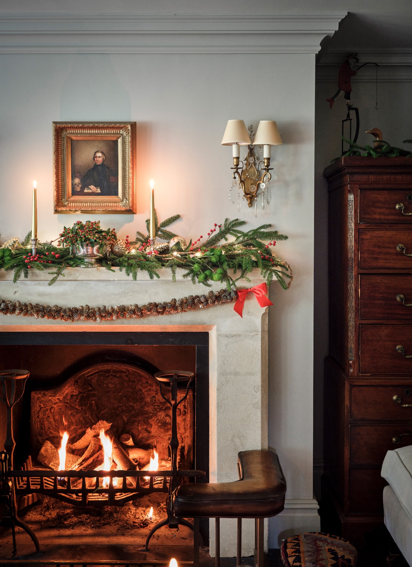 A stone fireplace decorated with a lush spruce garland and a draped pinecone swag above a crackling fire