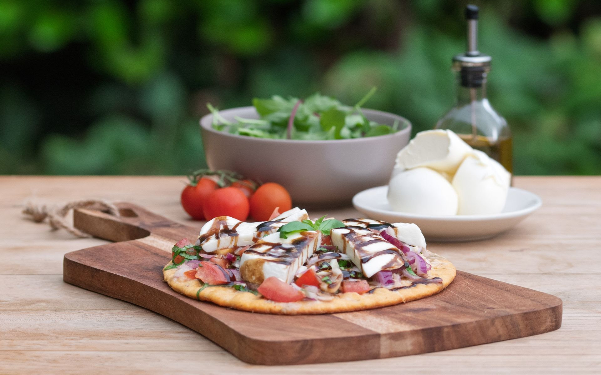 a bruchetta and mozarella flatbread on a wooden serving board on a garden table