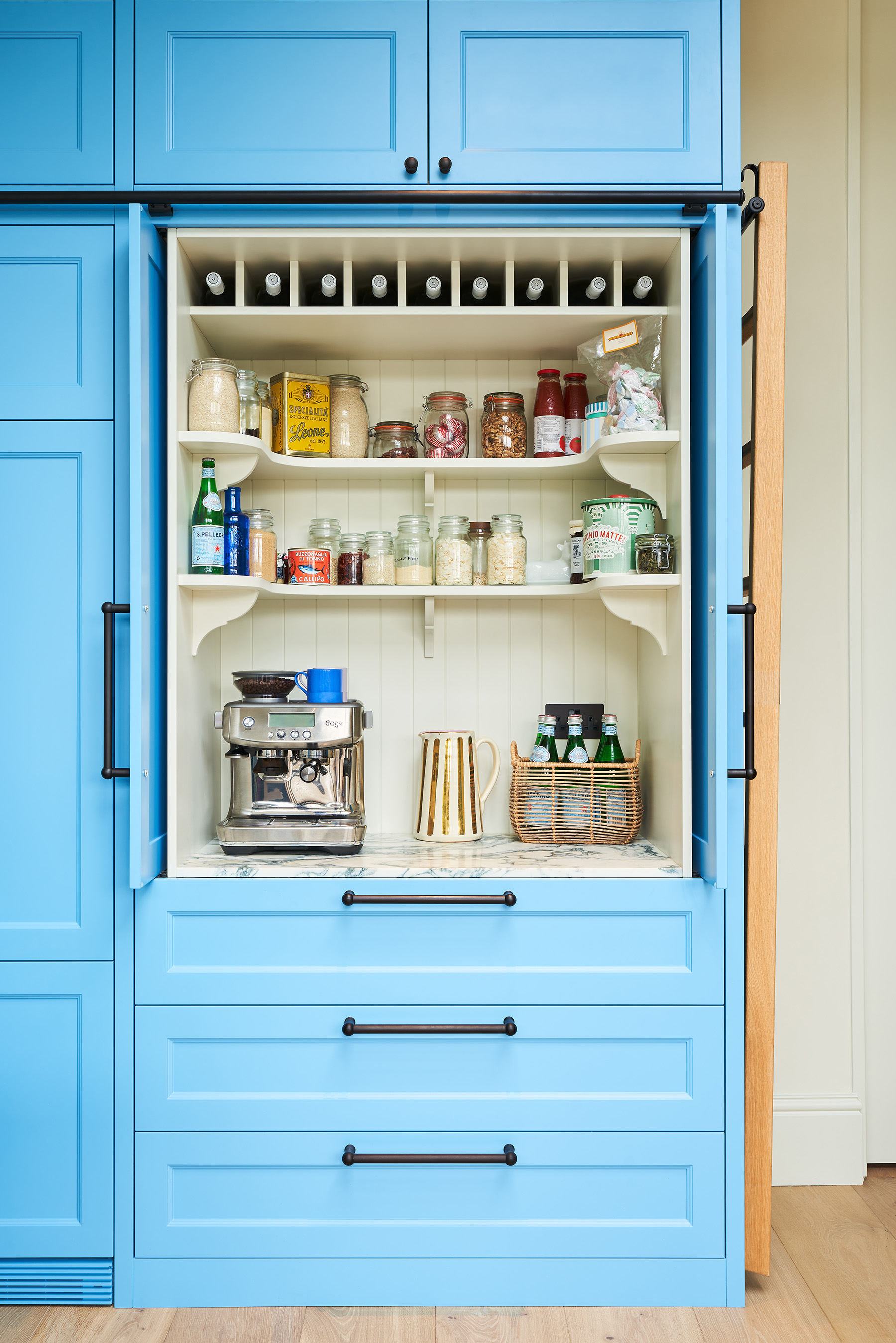 dedicated breakfast cupboard in tall, built-in kitchen cabinet in blue, storing wine bottles, kitchen jars and a coffee machine 