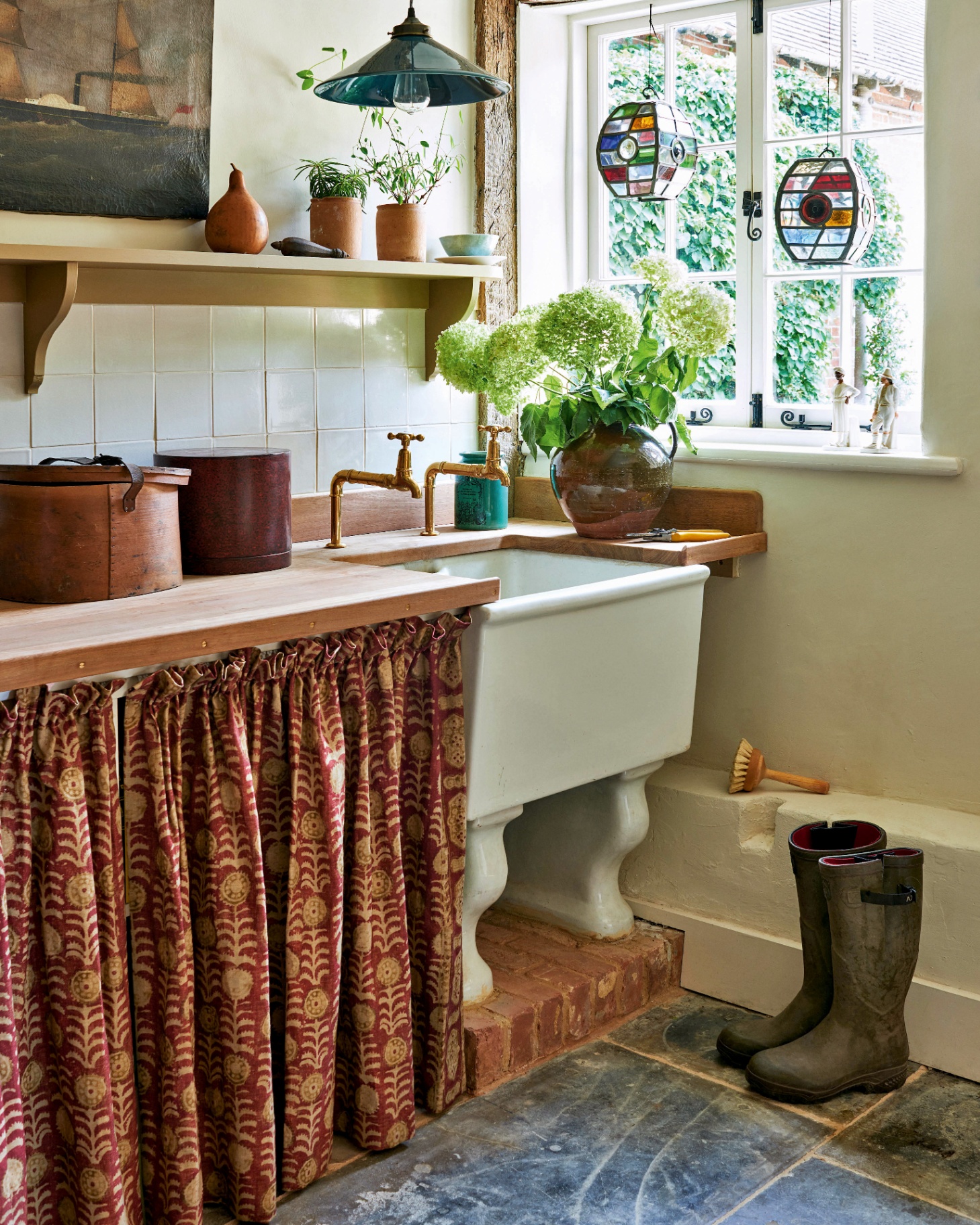 a traditional utility room with dark stone floors, a red and beige patterned fabric skirt concealing a cupboard and a large white belfast sink with space underneath