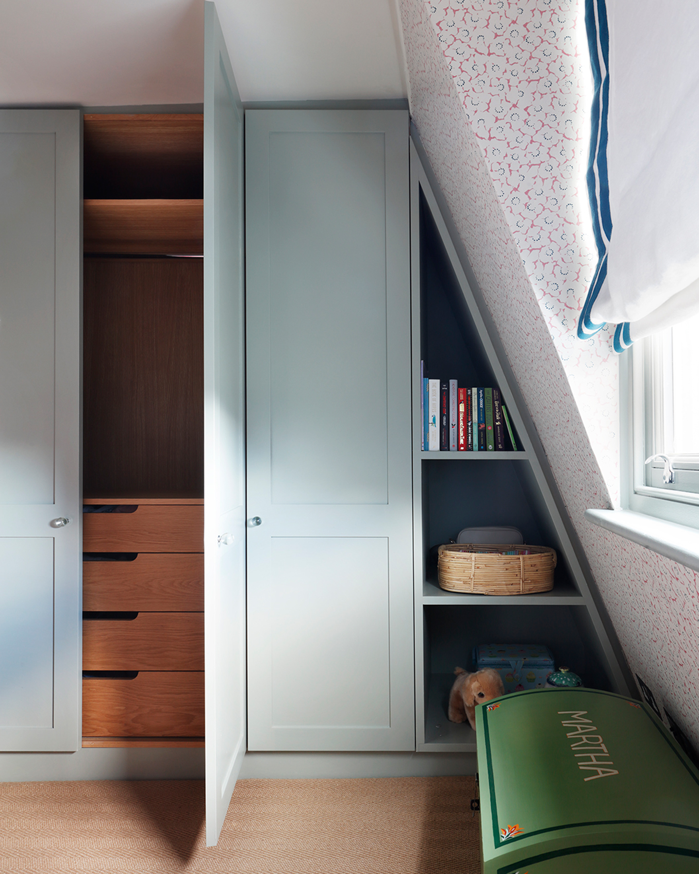 a bedroom with pale blue built in wardrobe, a green toy box and a white and red and blue floral wallpaper