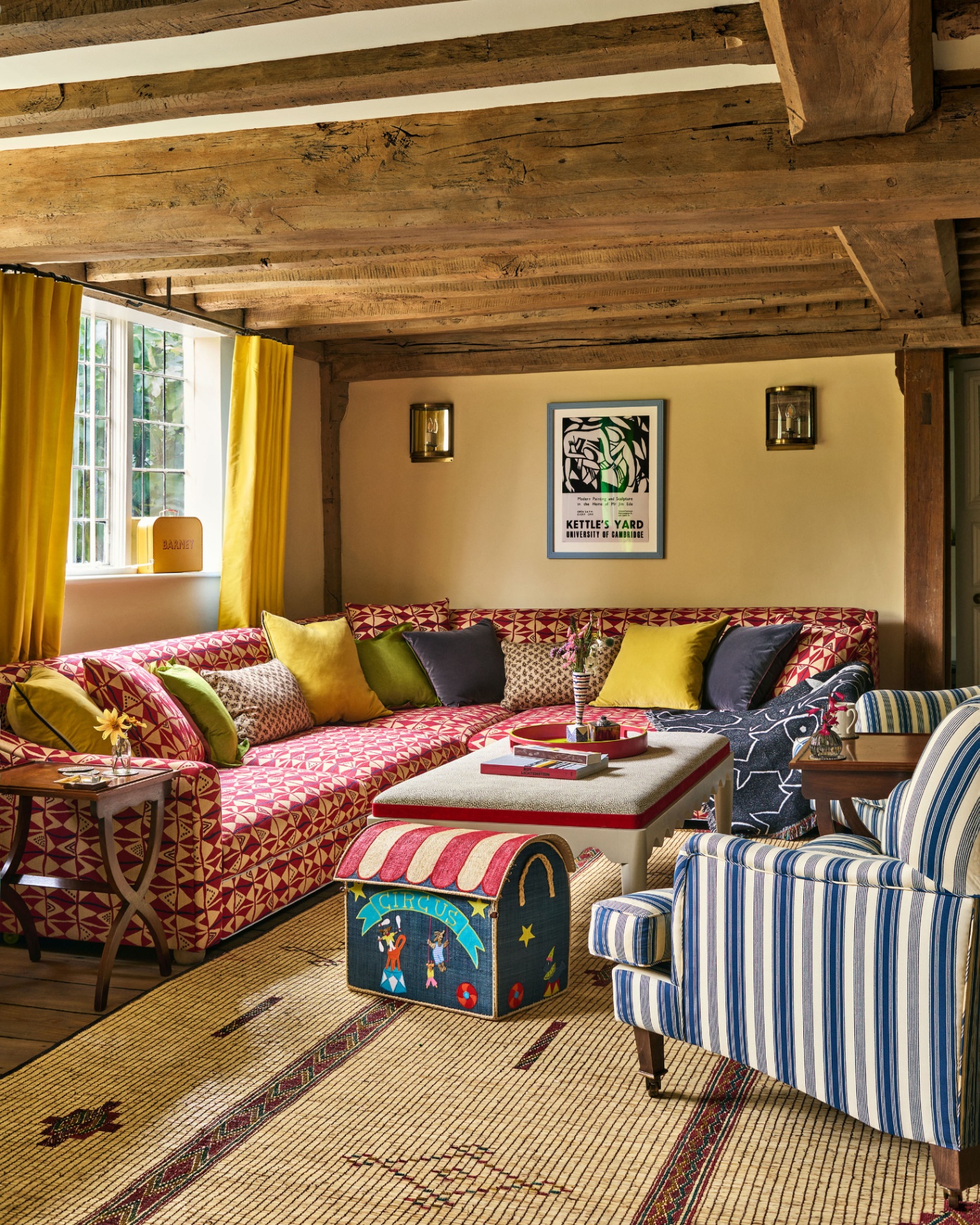 a living room with wooden beams, a large red and white patterned l shaped sofa with yellow and green cushions and a blue and white stripe armchair in the corner