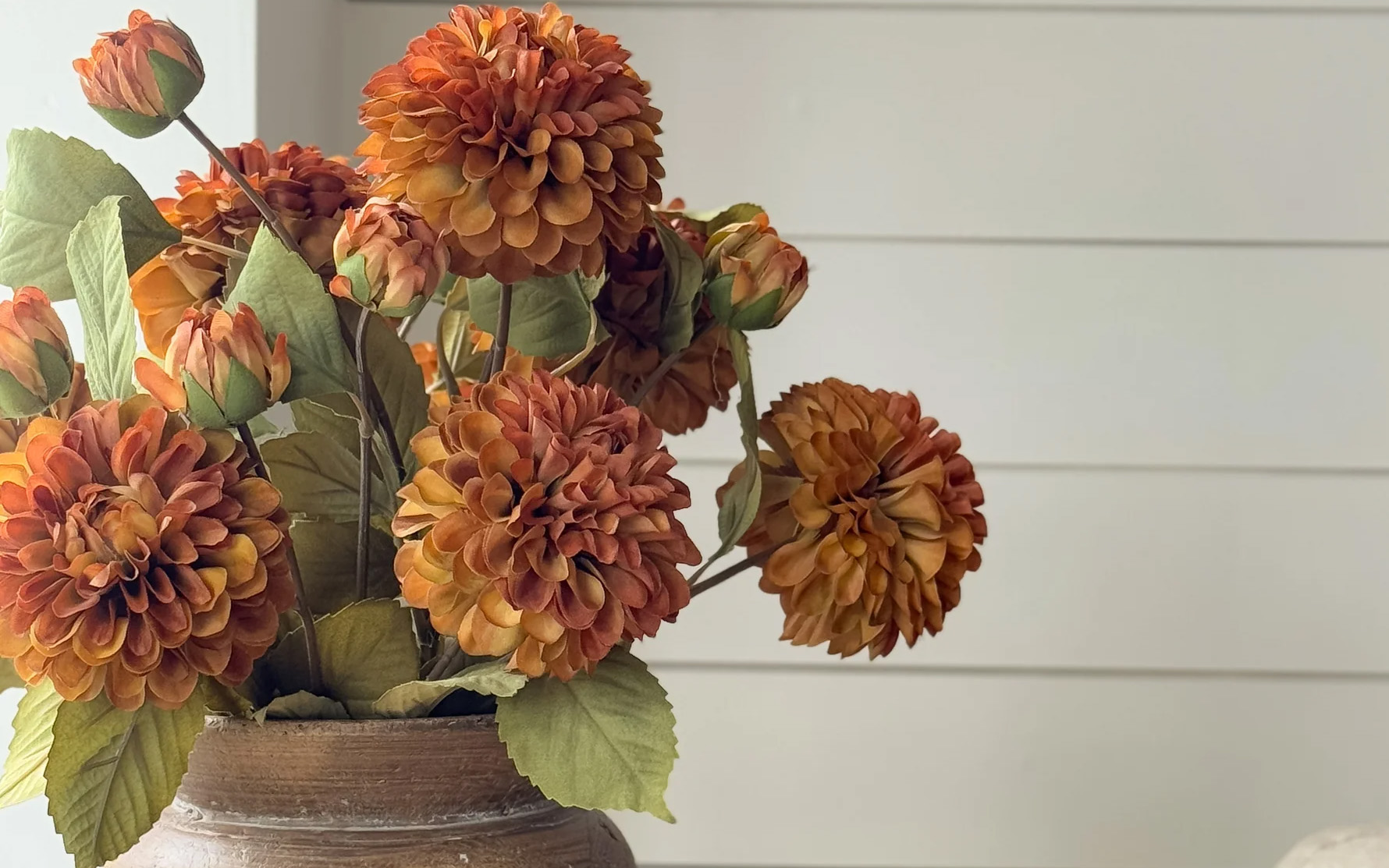 a bunch of burnt orange faux dahlias in a beige stone vase