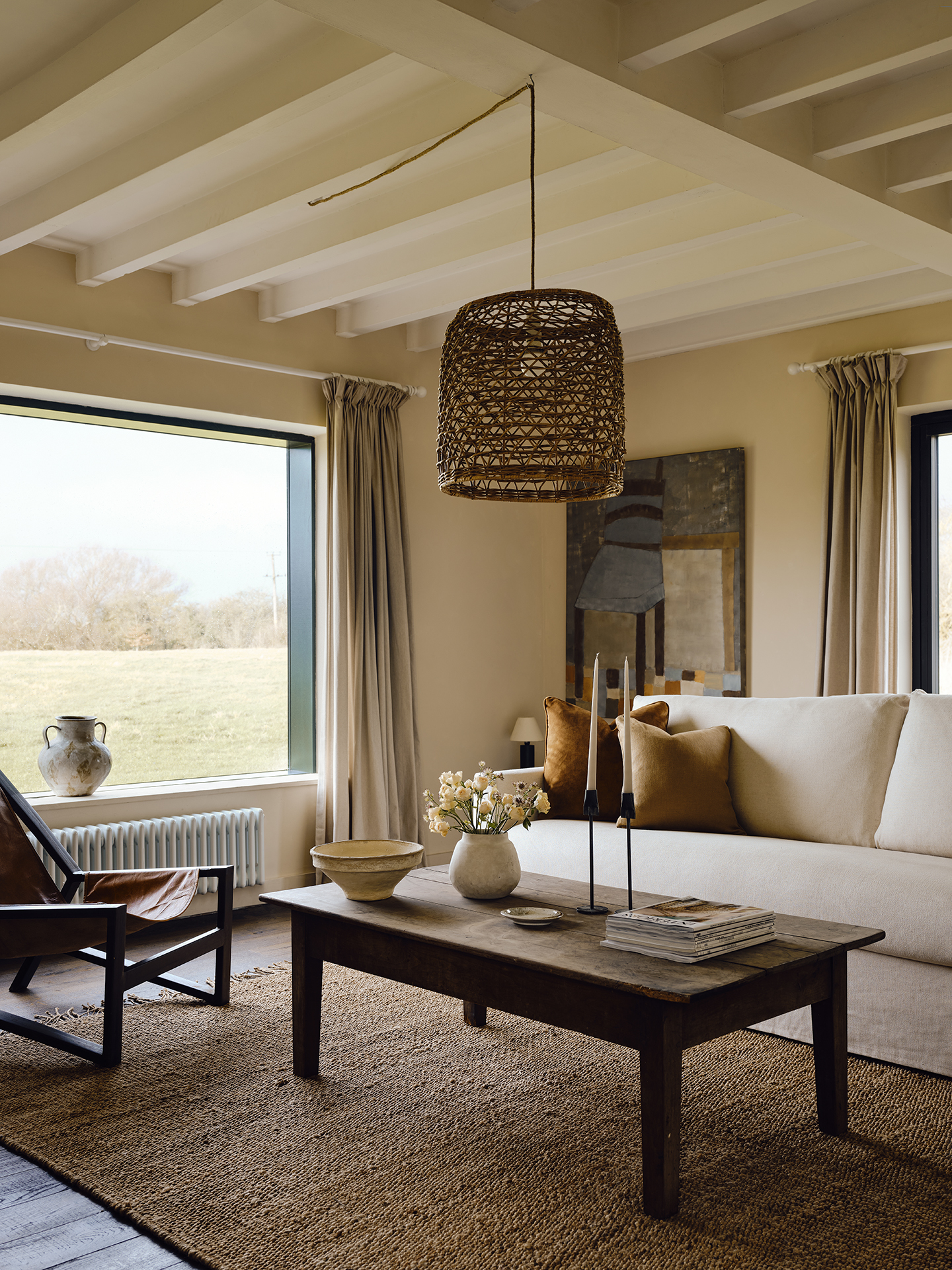 A white sofa and contemporary accent chair are arranged around a wooden coffee table on a large jute rug in this living room. A large rattan pendant hangs above. 