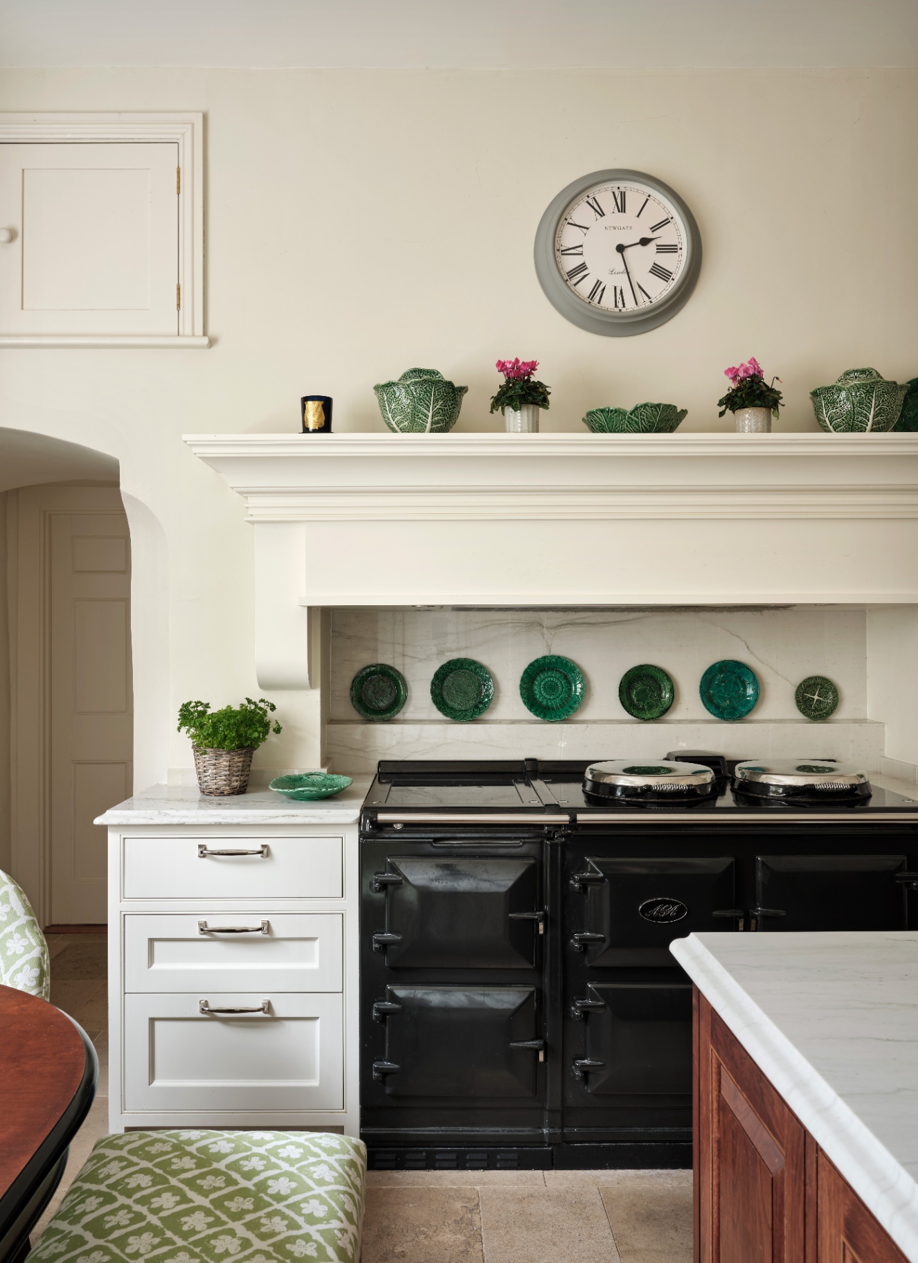 a kitchen with white walls, green decorative paltes on a shelf and a large black aga