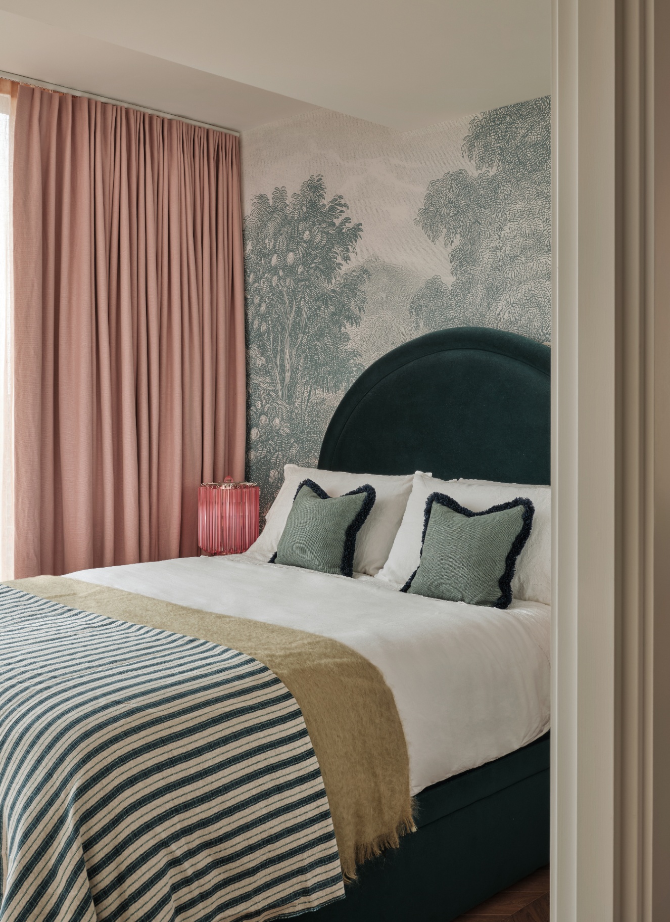 a bedroom with white and teal botanical wallpaper and a bed with a velvet teal headboard and a stripe bedspread