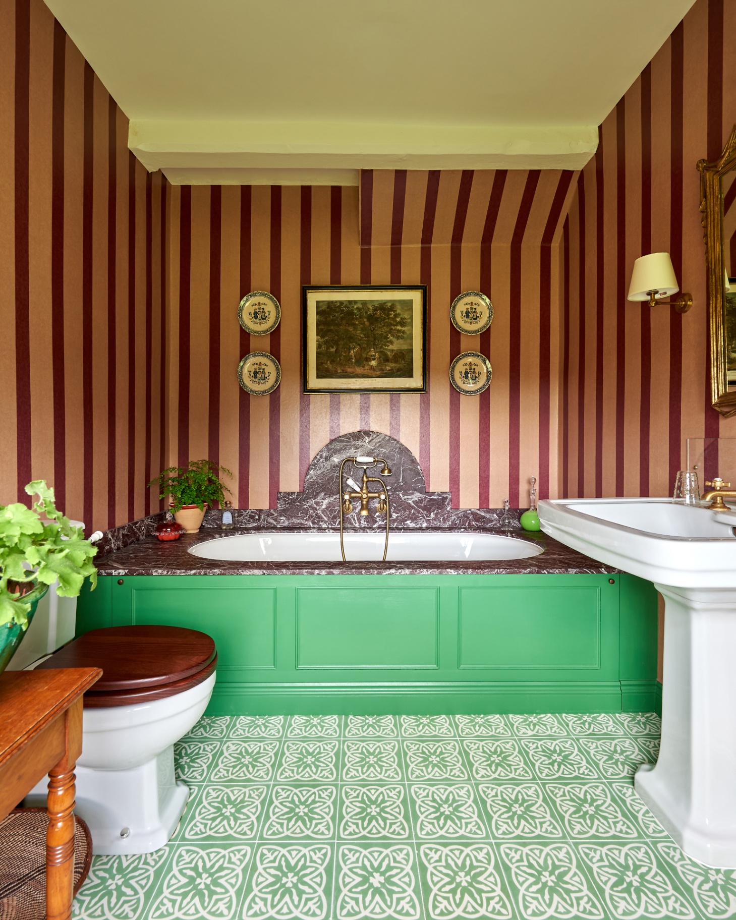 a bathroom with pink and red striped wallpaper, green and white patterned floor tiles and a green and marble bath tub