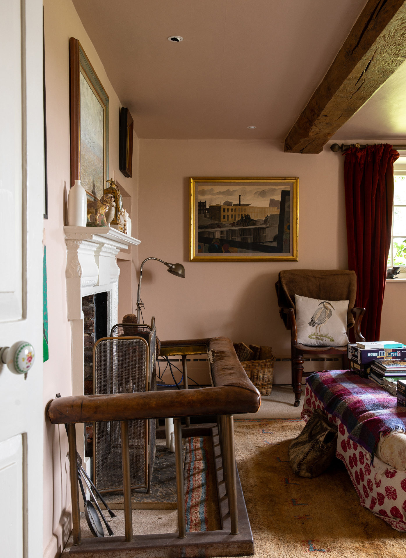 a cottage living room with plaster pink walls and wooden beams on the ceiling, a large leather fire surround and a large framed painting in a gold frame