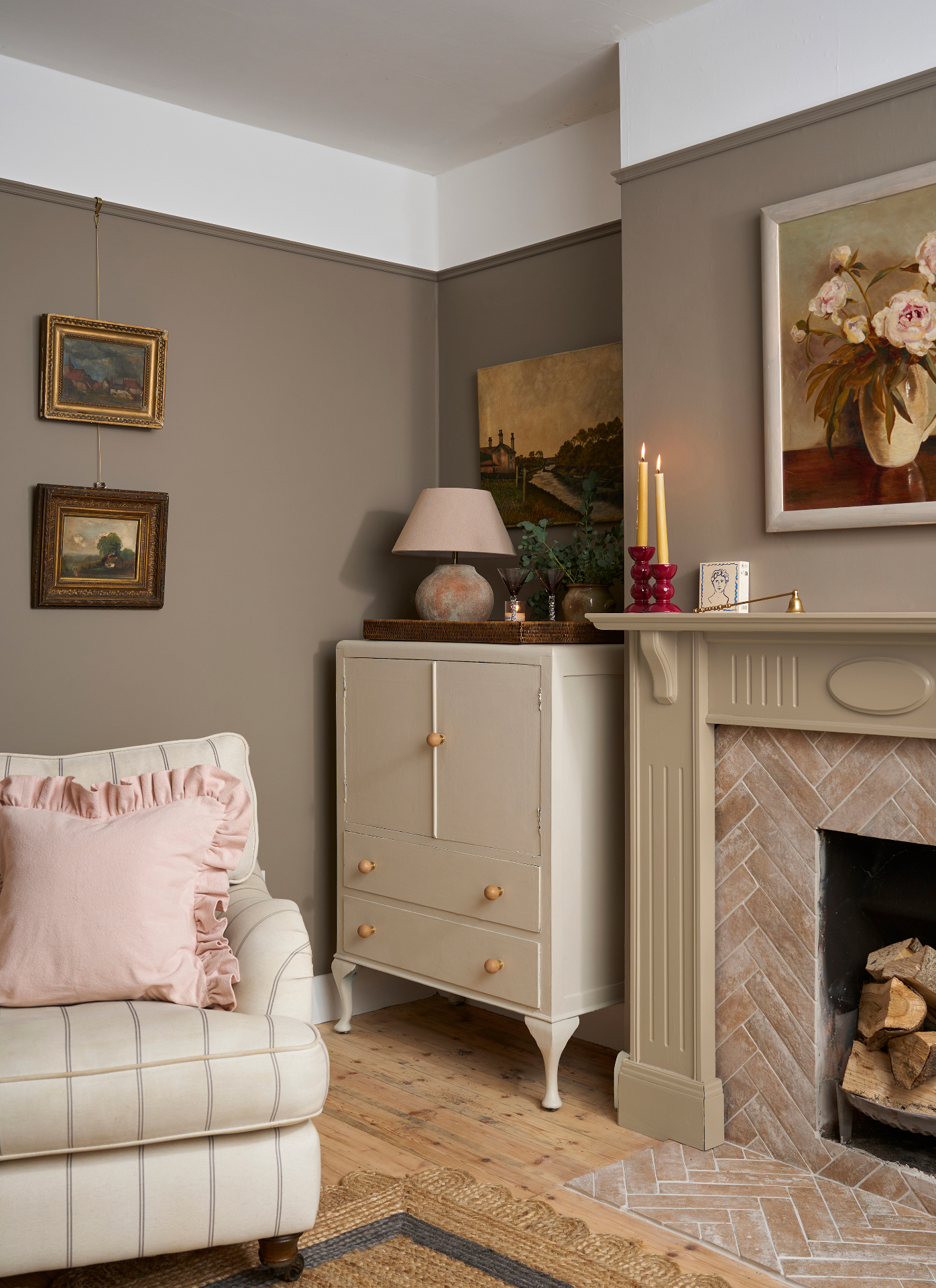 a living room corner with pale brown walls, a brick fireplace, a cream dresser and a white and stripe armchair