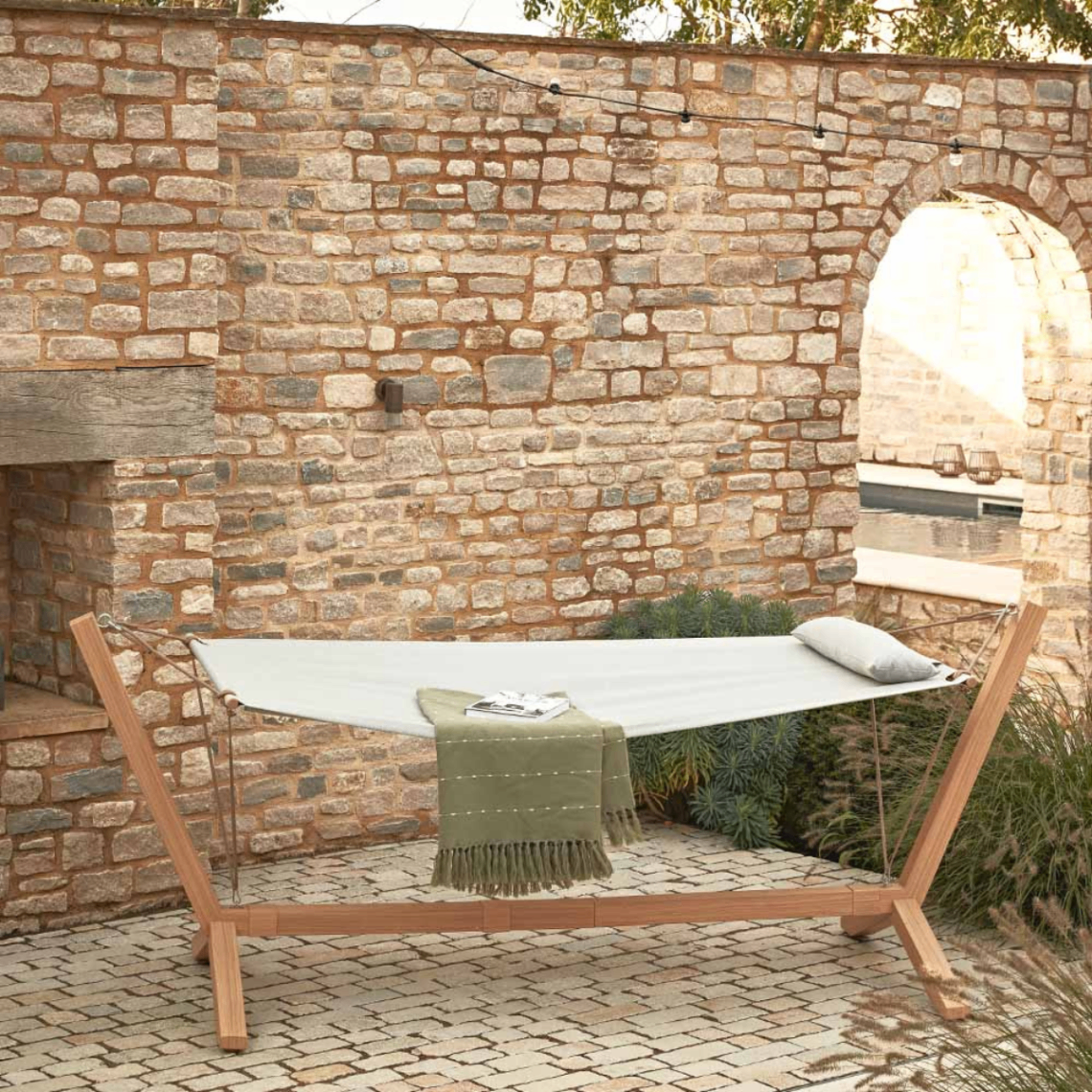 a cream hammock on a wooden stand with a green blanket on it in front of a stone wall