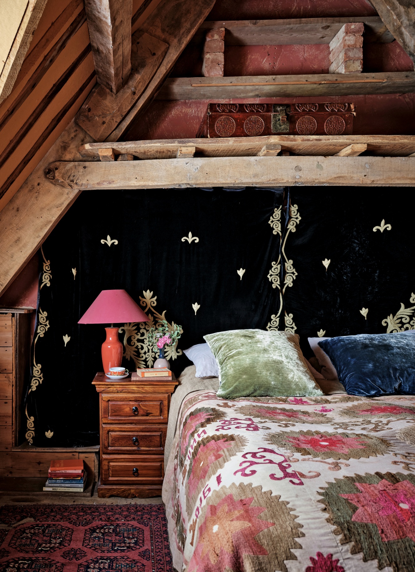 Attic bedroom under exposed wood beams featuring a dark fabric headboard wall with gold star accents, a pink lampshade, and a patterned quilt with plush pillows