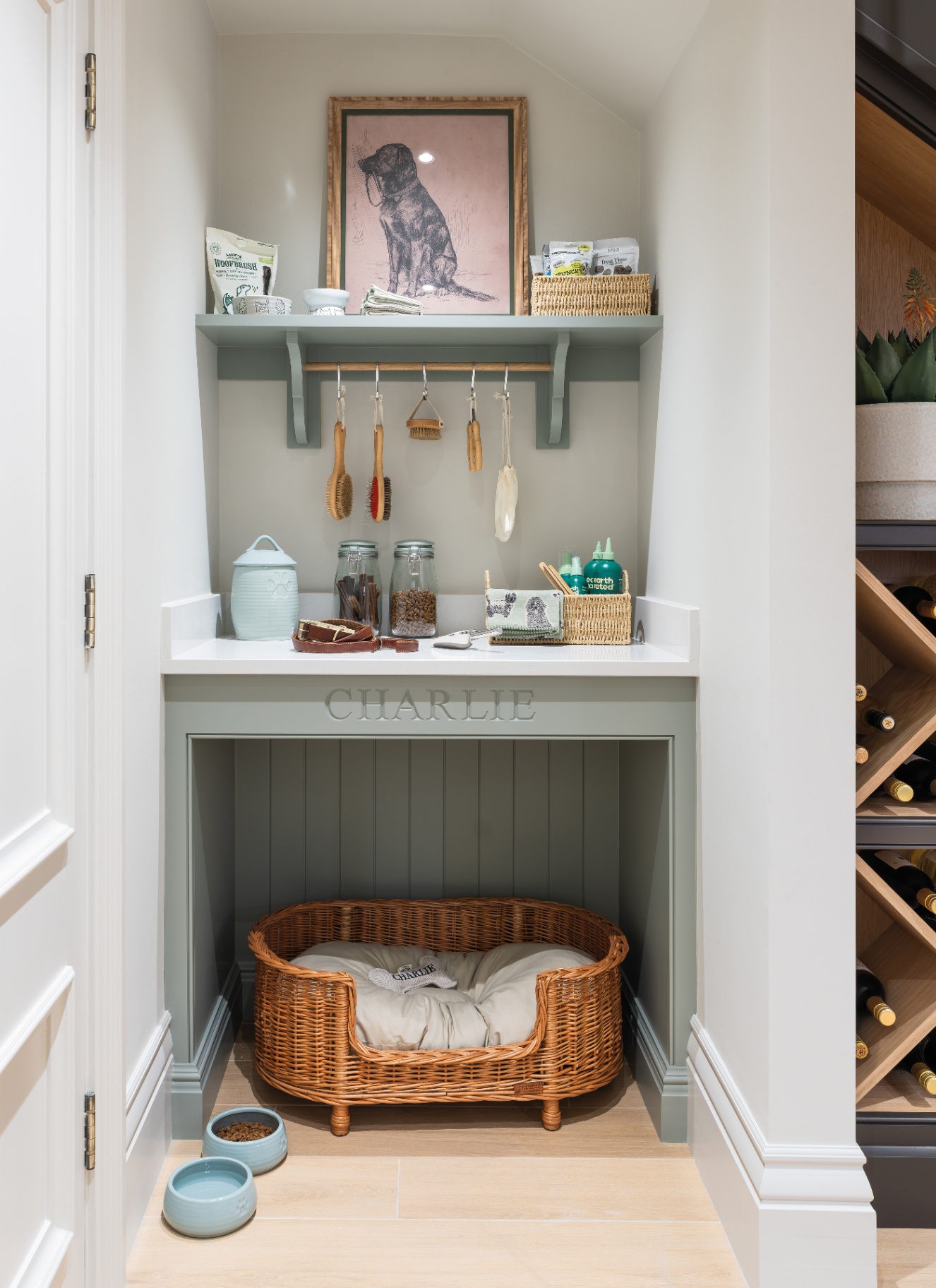 a dedicated pet zone with a wicker bed in an alove, dog bowls on the floor and a wooden hanging rail above the bed with brushes hanging from it