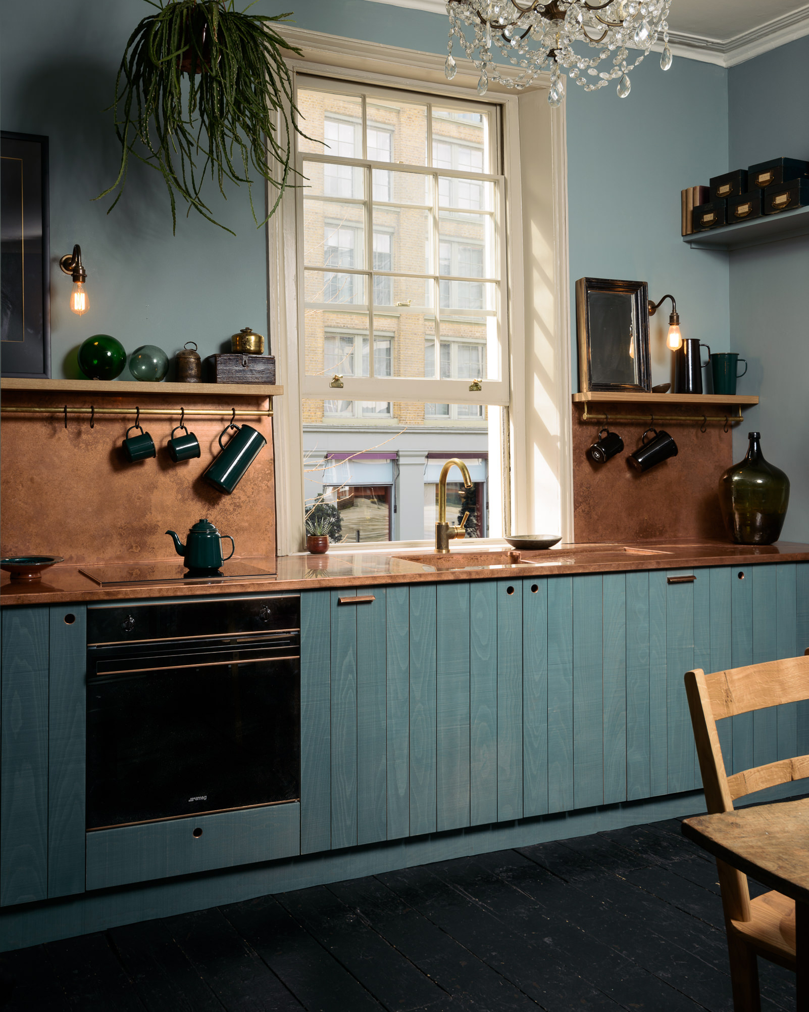 a dark kitchen with blue cabinetry and copper worktops and splashback