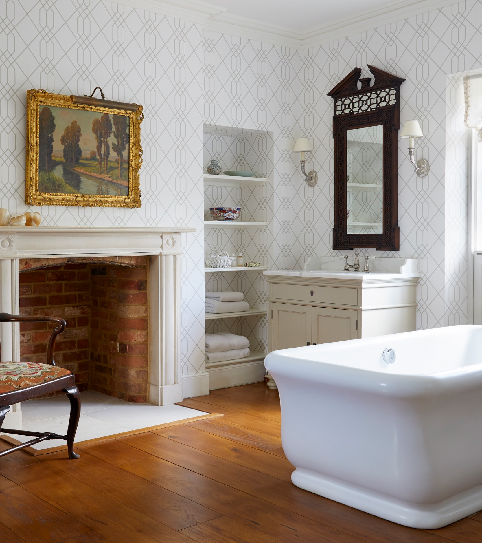 a bathroom with wooden floor, a white freestanding bath, a white fireplace with exposed brick inside, a cream vanity unit with a large antique wood mirror above