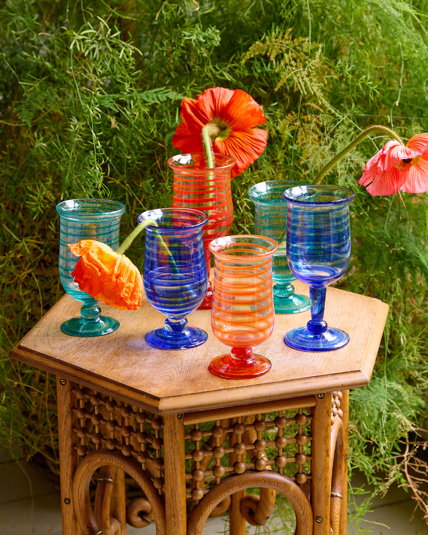 a wooden outdoor side table with colourful glasses on top with flower stems