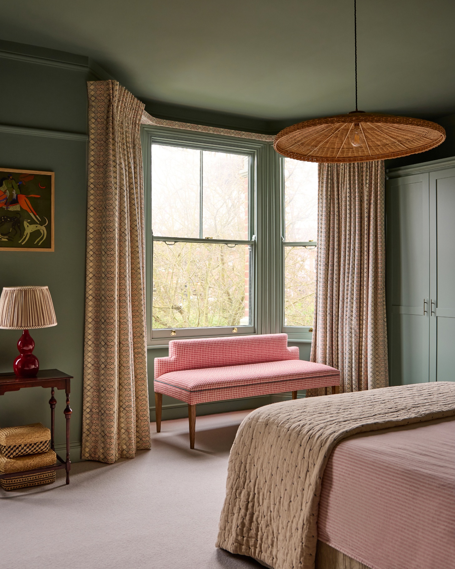 a bedroom with green painted ceilings and walls, a red gingham window seat, a large rattan pendant shade and a bed with a stripe sheet