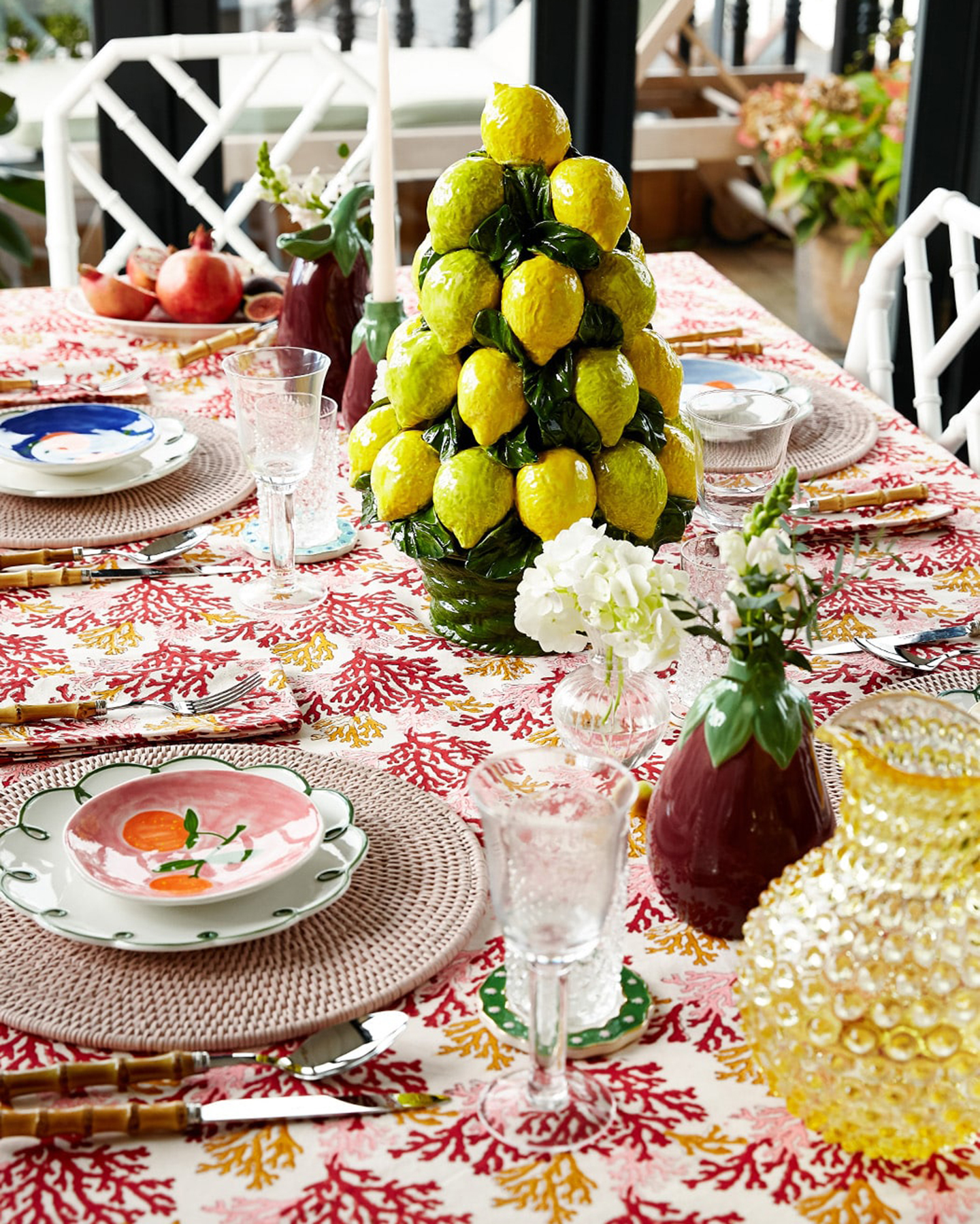 a summer table with a large lemon ceramic centrepiece, a coral patterned tablecloth, an aubergine vase and a yellow textured water jug