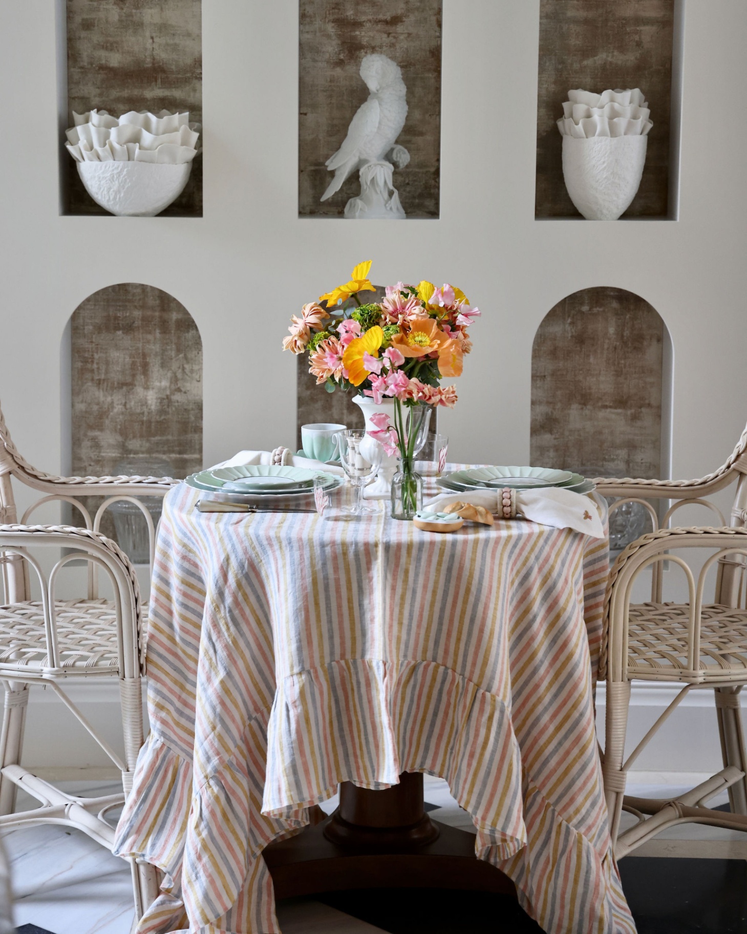 a round table with a pastel stripe and ruffle tablecloth with a large vase in the middle filled with colourful flowers