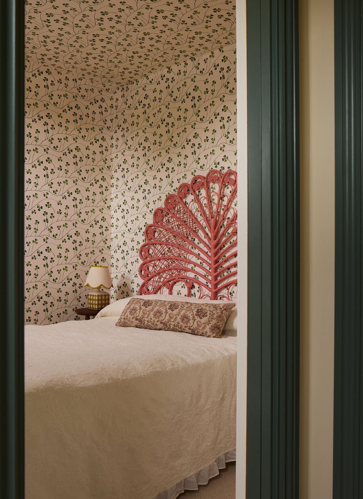 a bedroom with all over botanical wallpaper and a bed with a coral rattan headboard