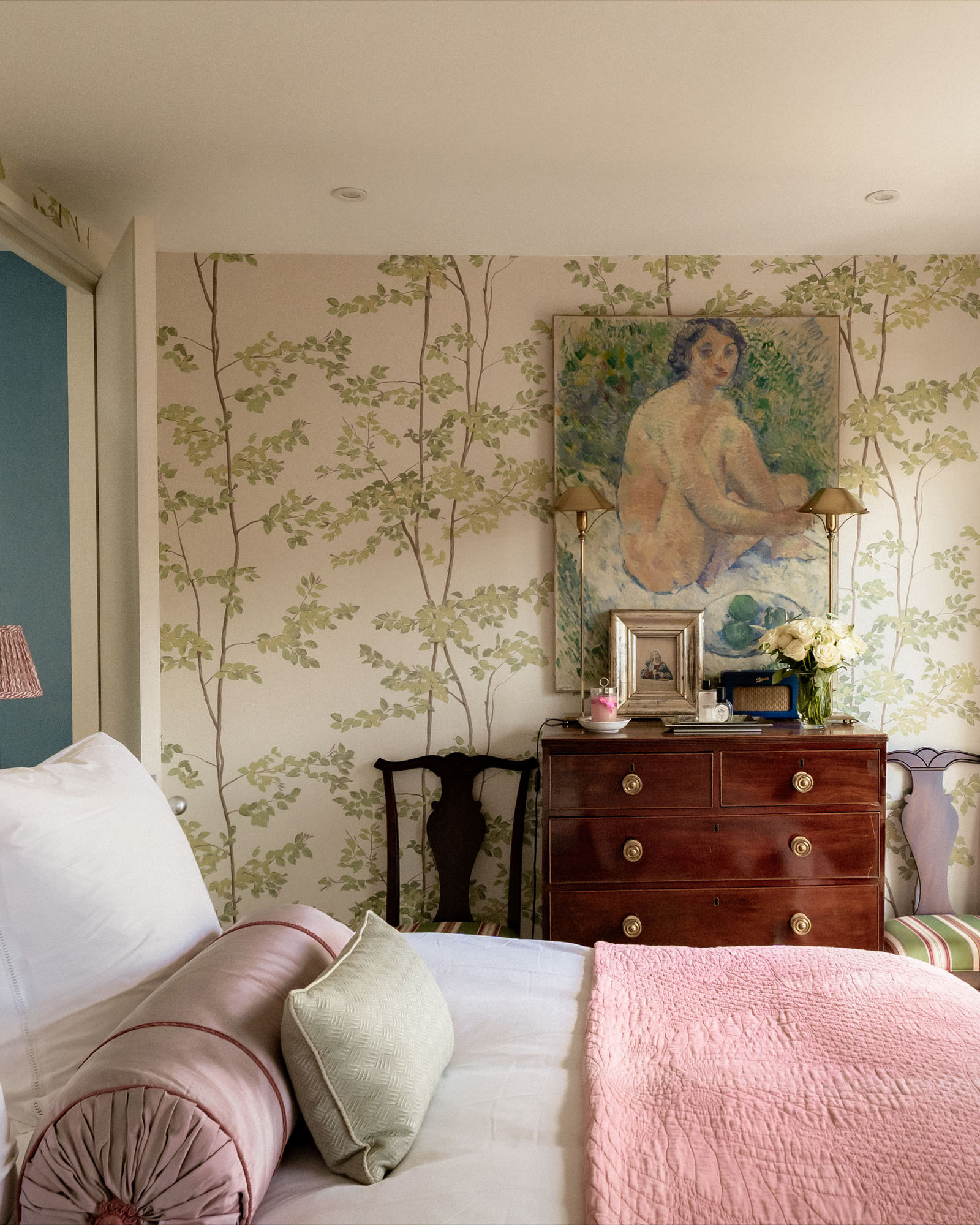 A BEDROOM with green botanical walls, a bed with white bedding and a pink bedspread and a large antique chest of drawers