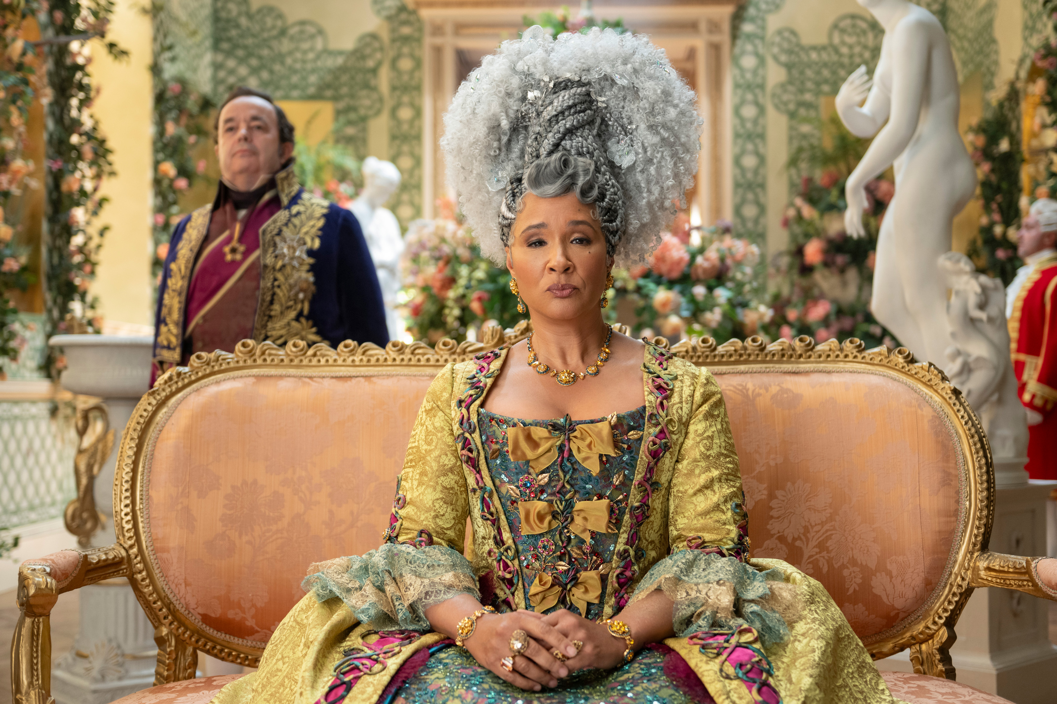 queen charlotte from season 4 bridgerton sat on a pale orange sofa surrounded by flowers