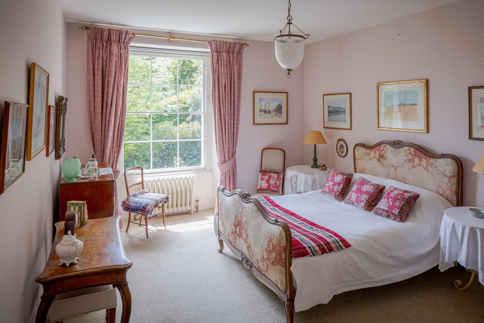a bedroom with pale pink walls, a large bed with a floral patterned headboard and pink curtains