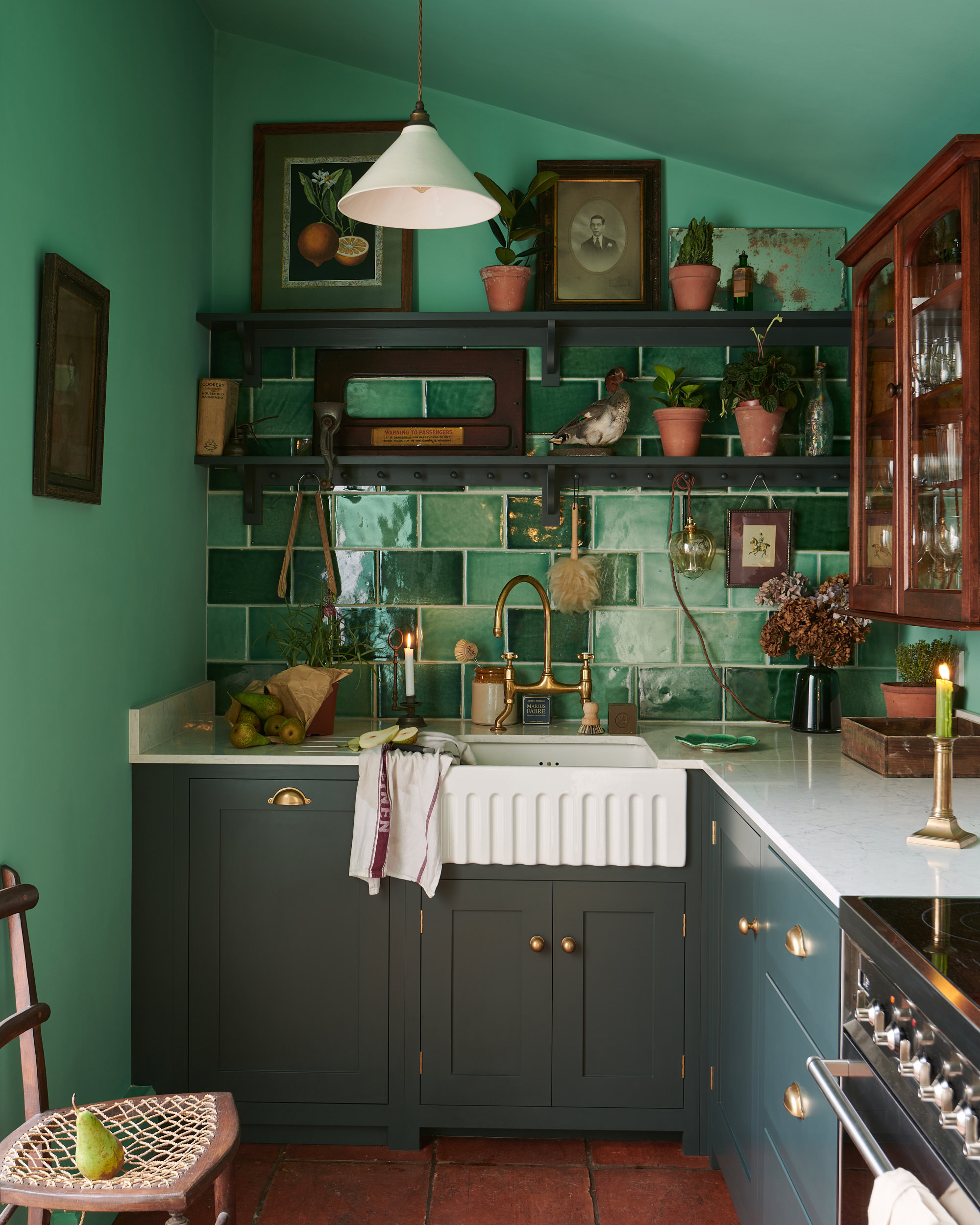 a green kitchen with green tiled splashback, dark green cabinetry, terracotta tile floors and open shelves