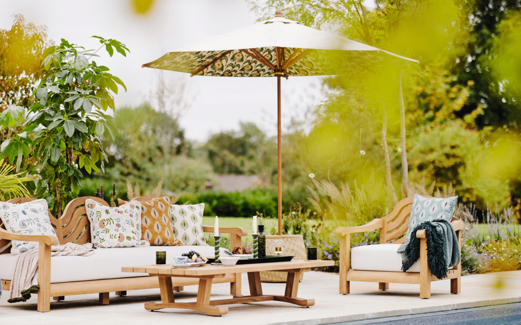 an outdoor area next to a pool, with a garden lounger and a neutral and patterned parasol