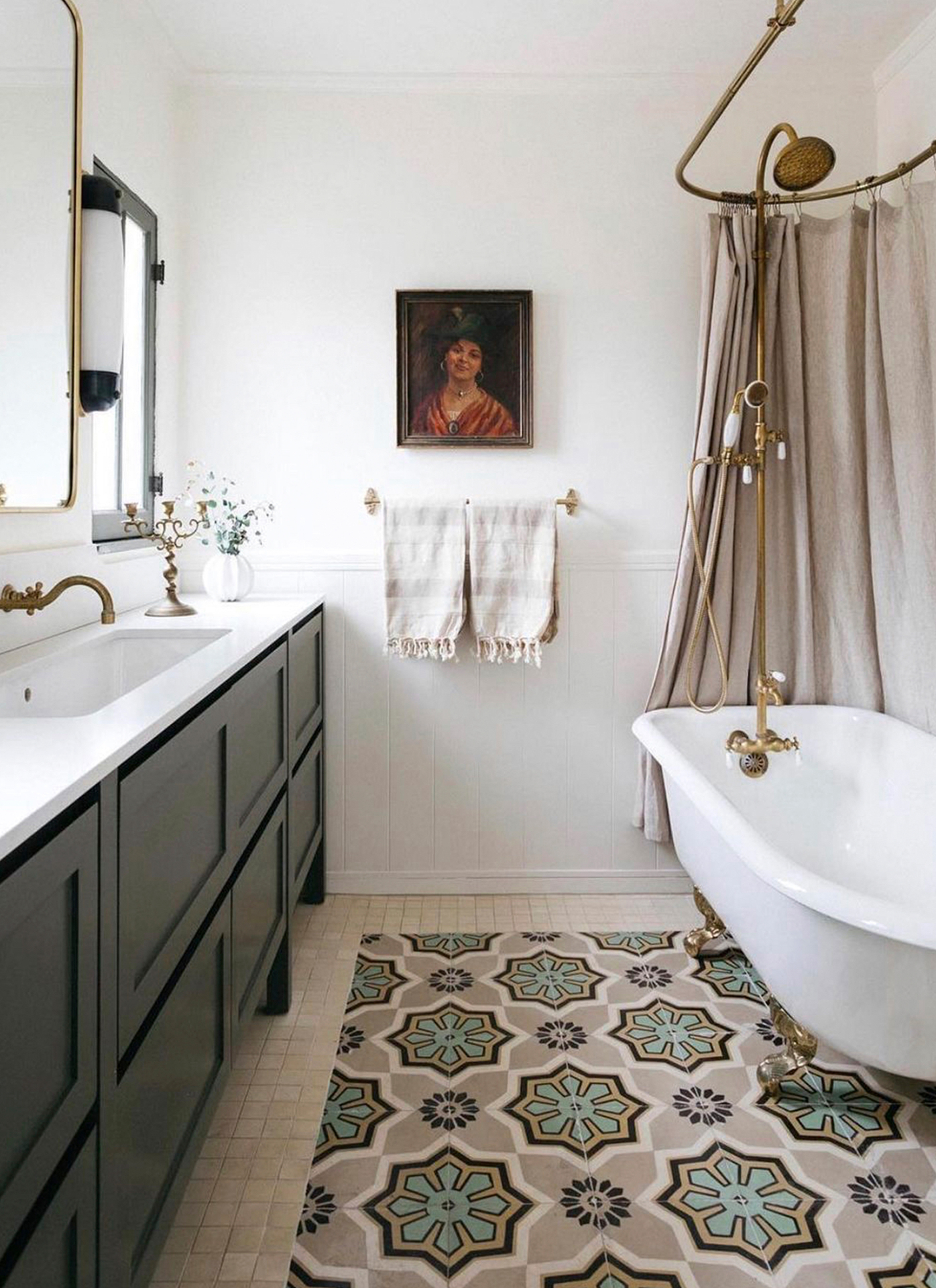 a bathroom with white walls, dark green vanity, a freestanding bath tub with gold hardware and a beige shower curtain and beige and green patterned floor tiles