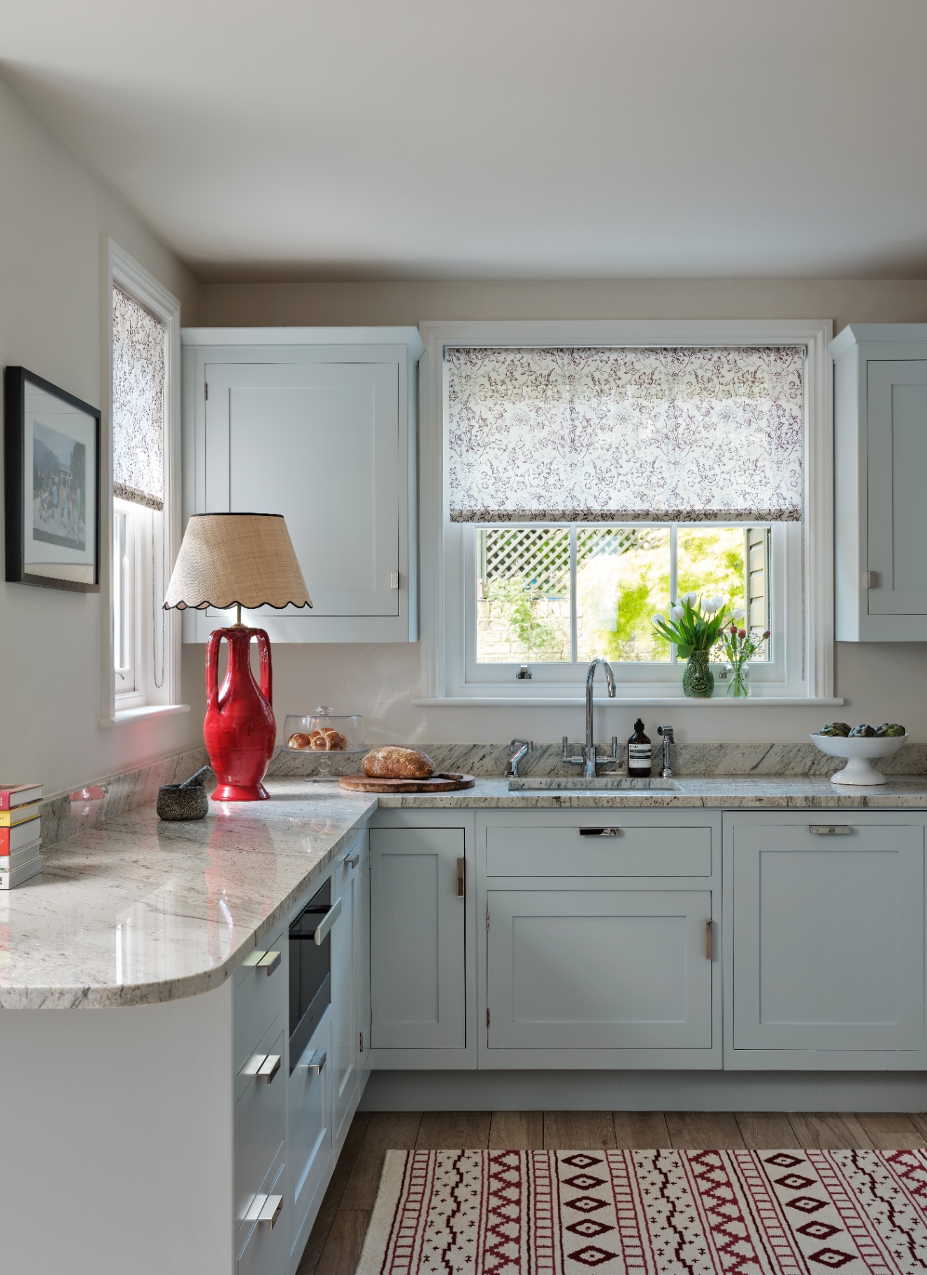 a kitchen with pale blue cabinetry, grey marble countertops and a red lamp