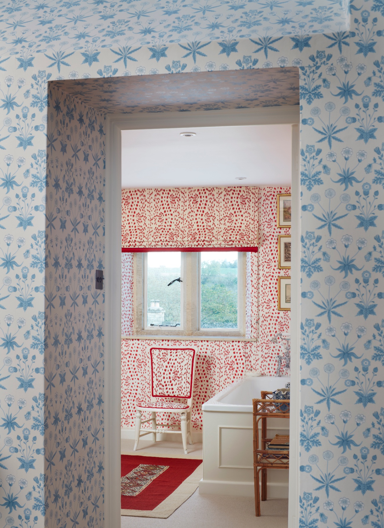 a room with white and blue floral wallpaper looking into a bathroom with white and red patterned wallpaper