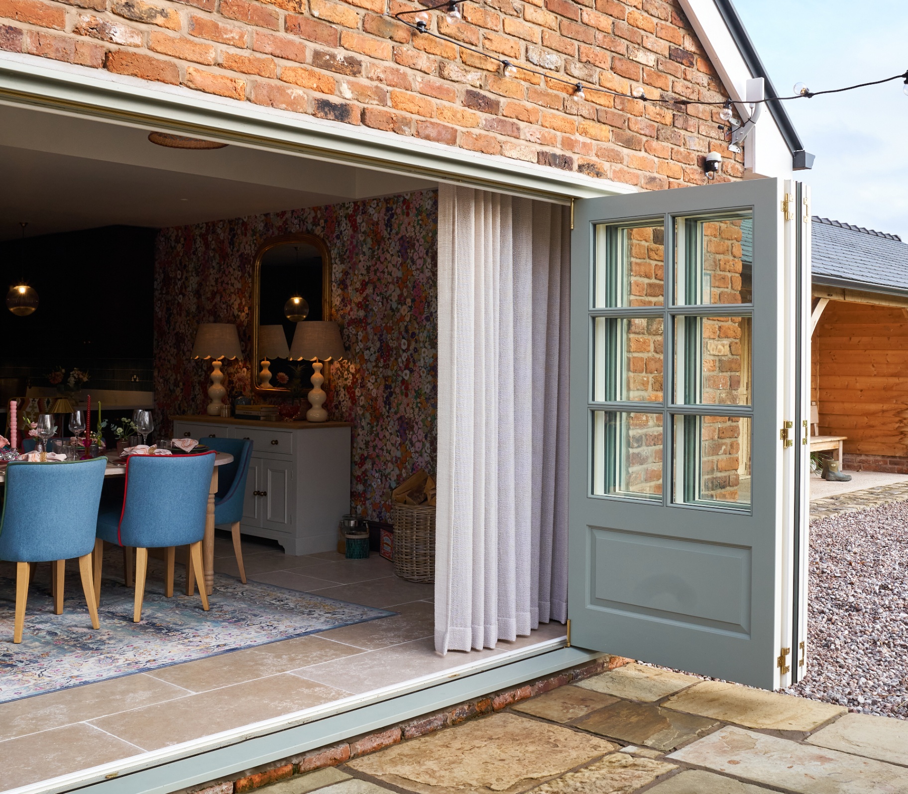 the exterior of a party barn converstion with red brick, an open sage green door and a dining table with blue chairs inside