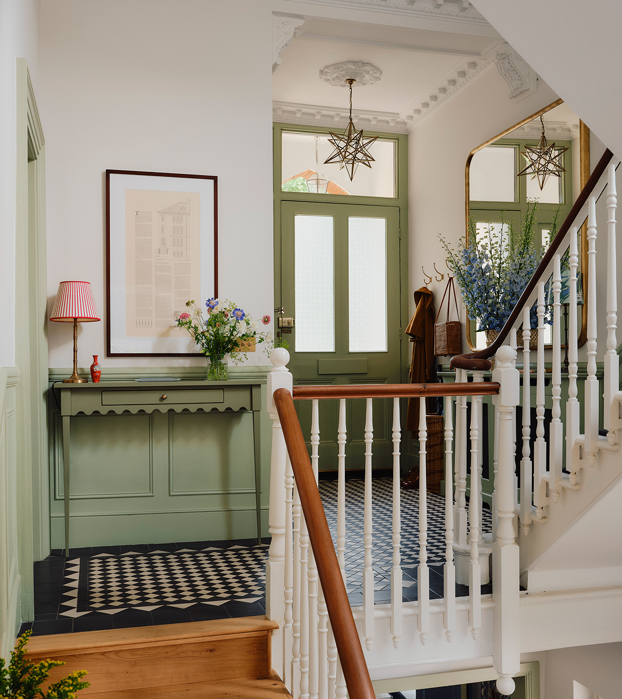 a large hallway with two toned white and green walls, a black and white floor, white and wood bannisters and a star shaped glass pendant