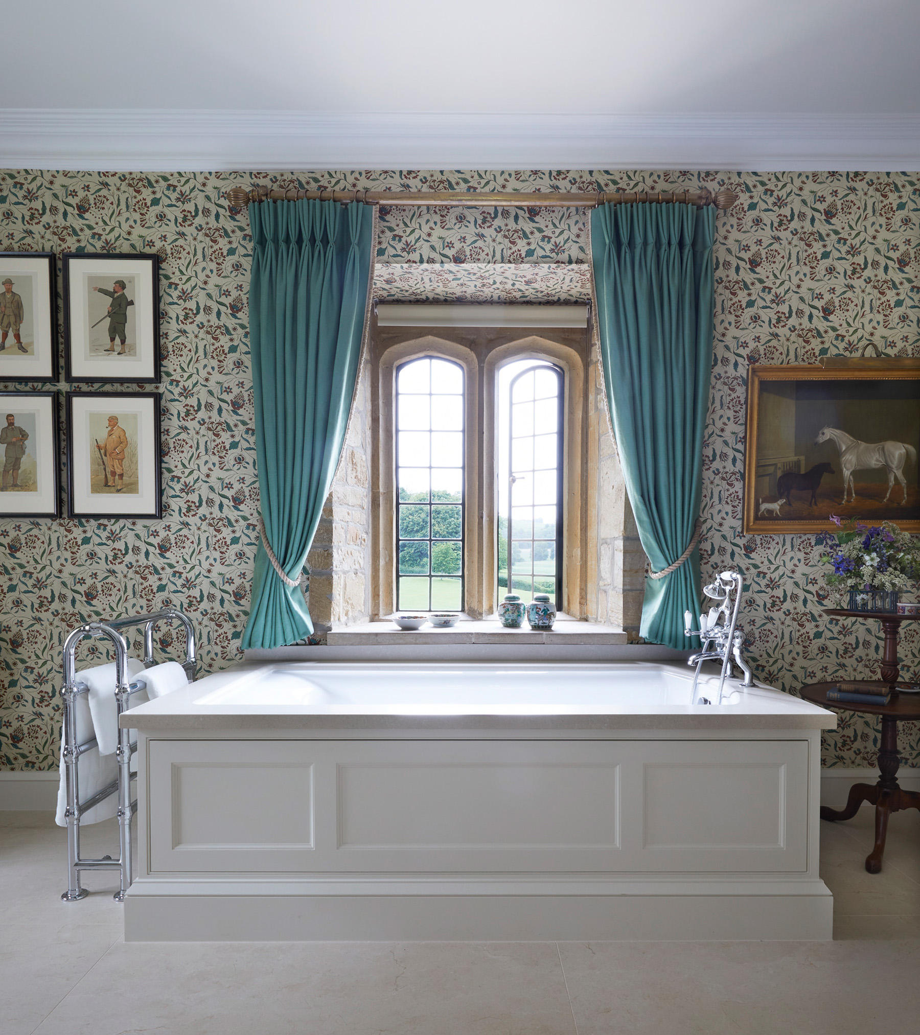 a bathroom with cream and red and blue floral wallpaper, an arched window with teal curtains and a large free standing bath