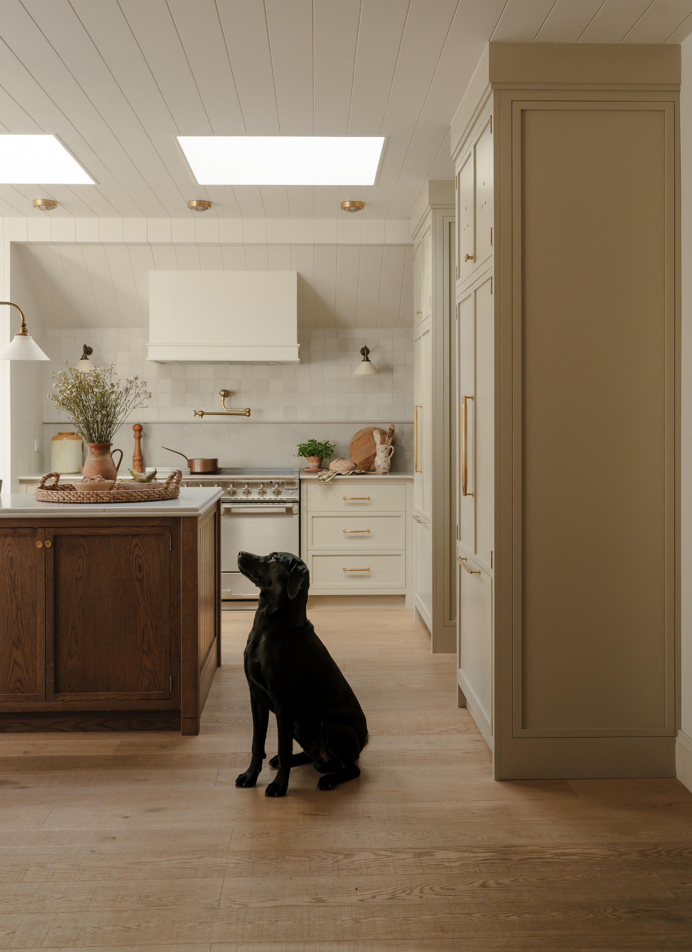 a kitchen with a black labrador sat on a wooden floor, a dark wooden kitchen island and off white cabinetry
