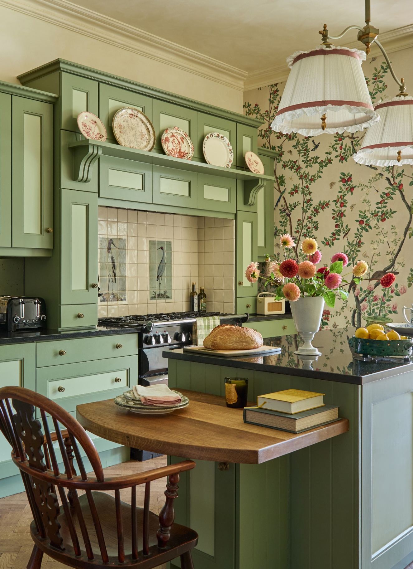 a country kitchen with sage green cabinetry, floral wallpaper and a sage green kitchen island with a drop leaf table