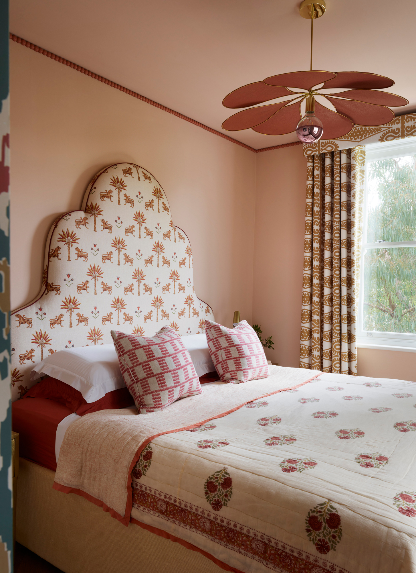 a bedroom with plaster pink walls, a pink flower shaped pendant light and a large bed with a patterned headboard
