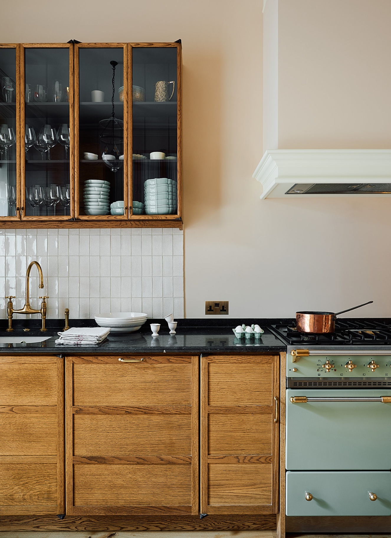 a kitchen with wooden cabinetry, a glass front floating cabinet and a sage green range cooker
