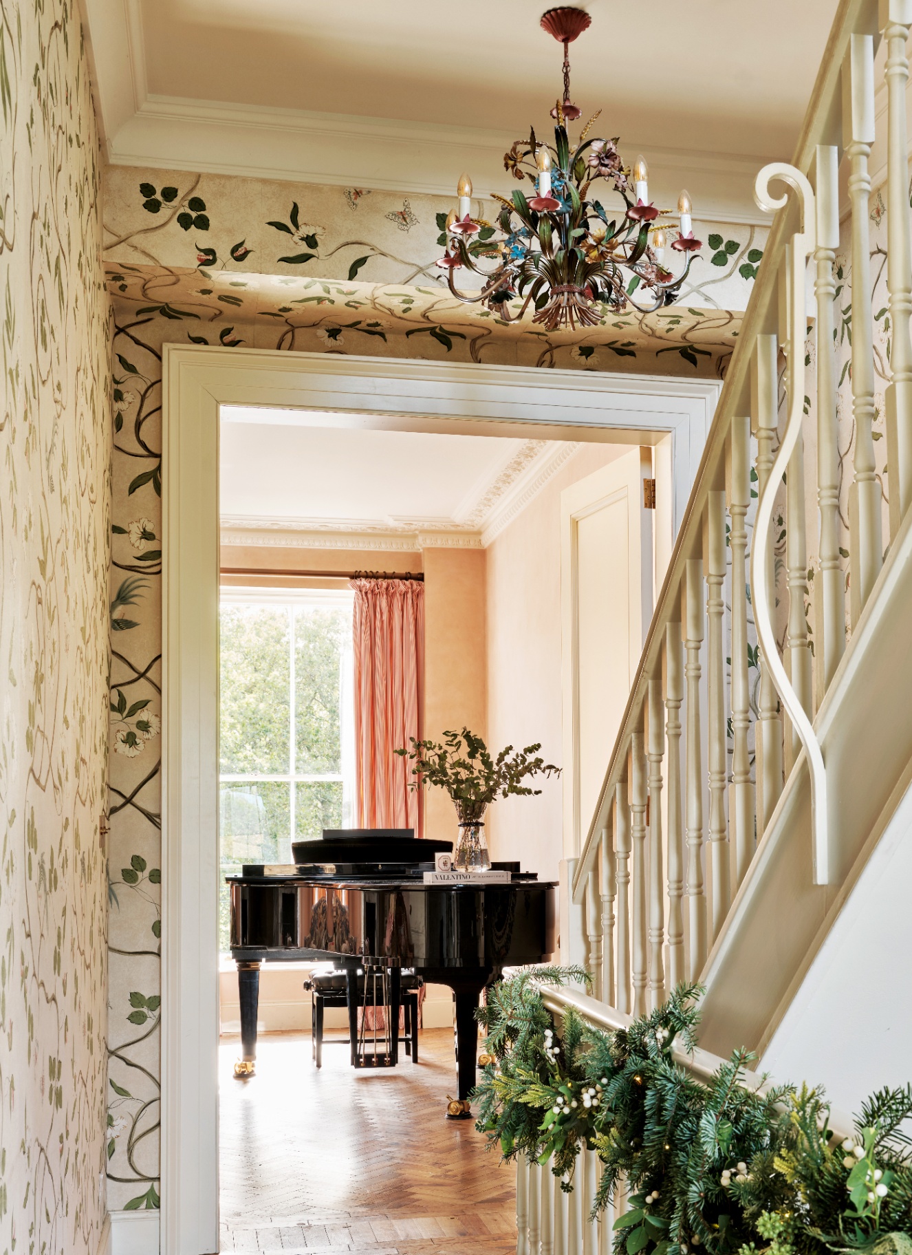 a hallway with white and green botanical wallpaper, a grand piano and an ornate chandelier