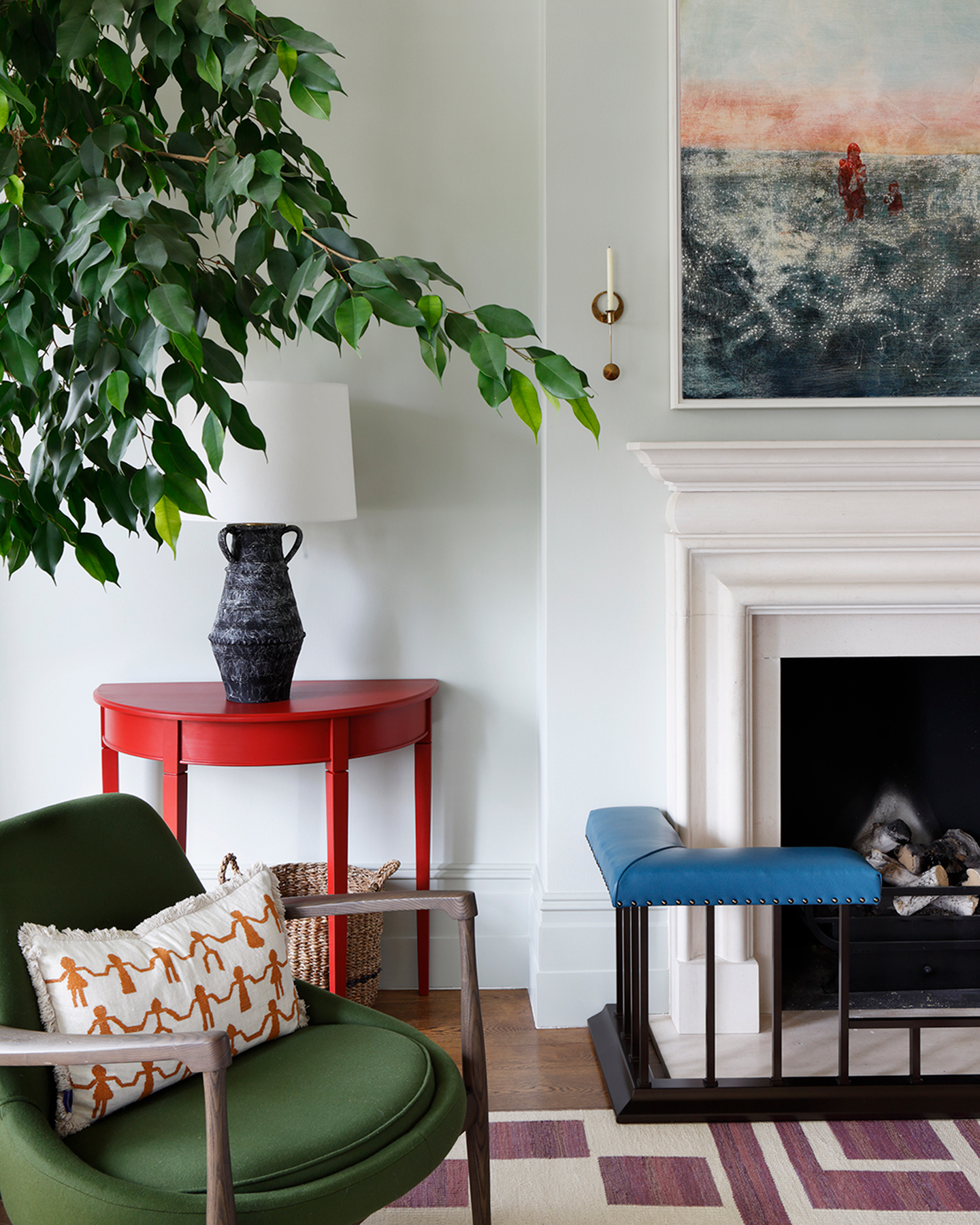a living room corner with white walls, a bright red painted console table, a green armchair, a large fireplace with a blue leather surround