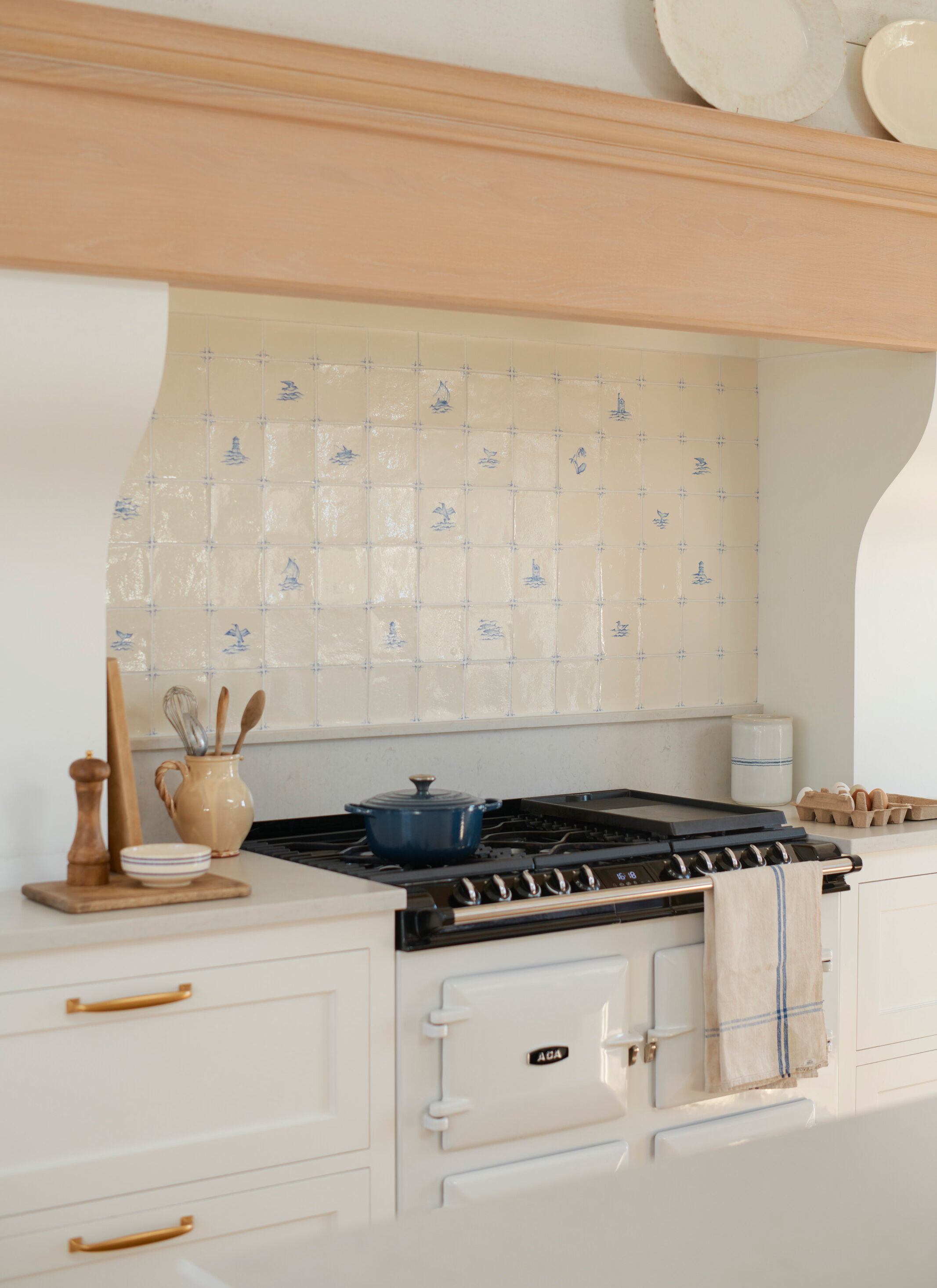 a cream range cooker with a peach painted mantel above it and delft tiles behind it