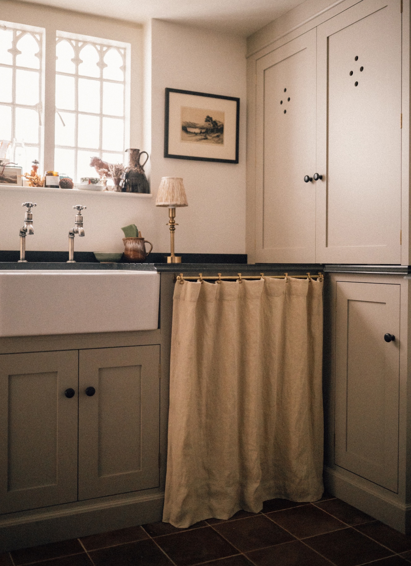 a utility room corner with grey cabinets, a cream sink skirt and a belfast sink