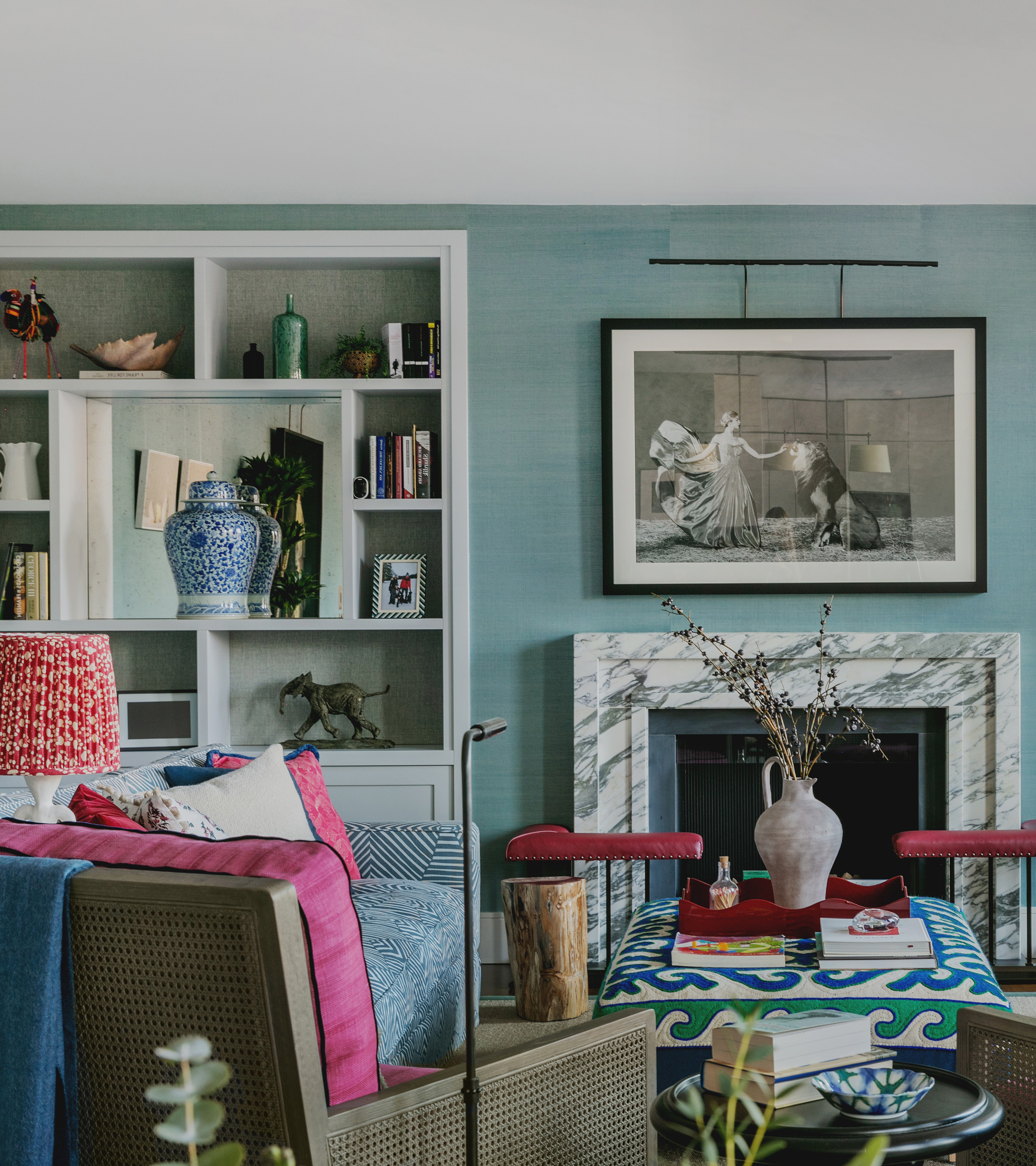 a living room with pale blue wall, a floor to ceiling white bookshelf to the left and a large marble fireplace to the right with a large black framed black and white photo above