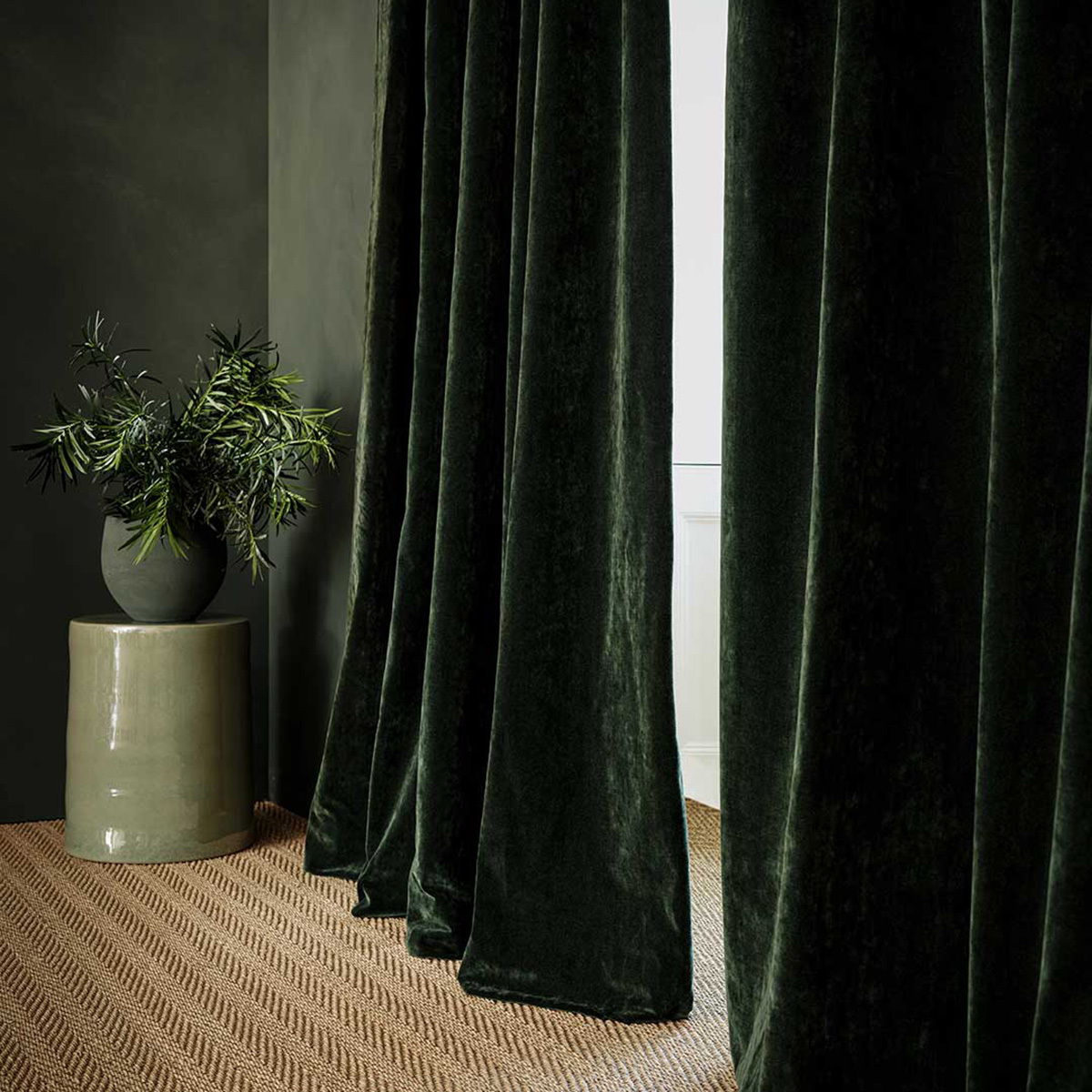 green walls with a vase and long dark green velvet curtains