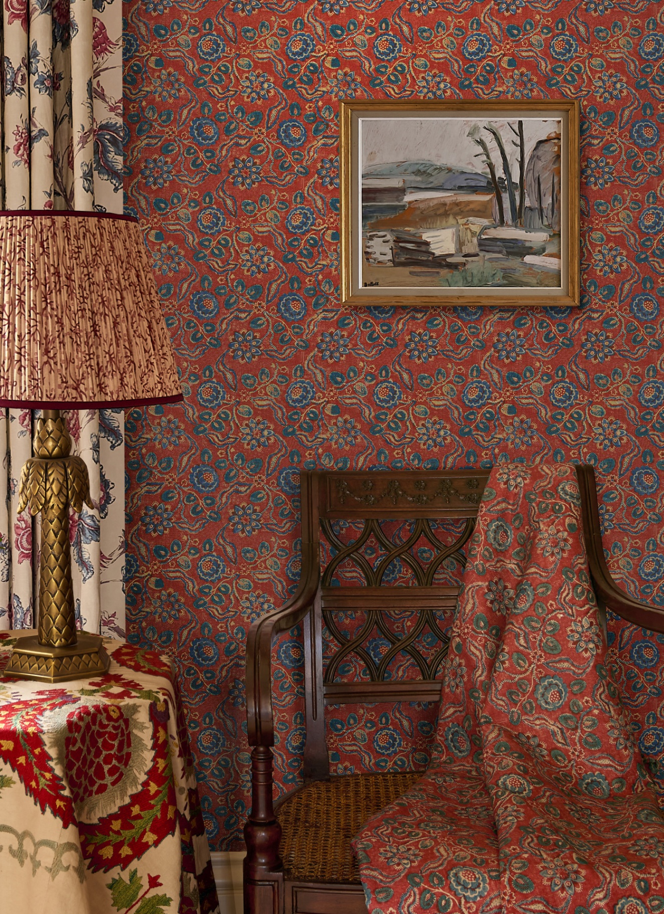 close up of an area of a room with red patterned wallpaper and a matching throw draped over an antique wooden dining chair and a red pleated lamp with a gold palm tree base on a table