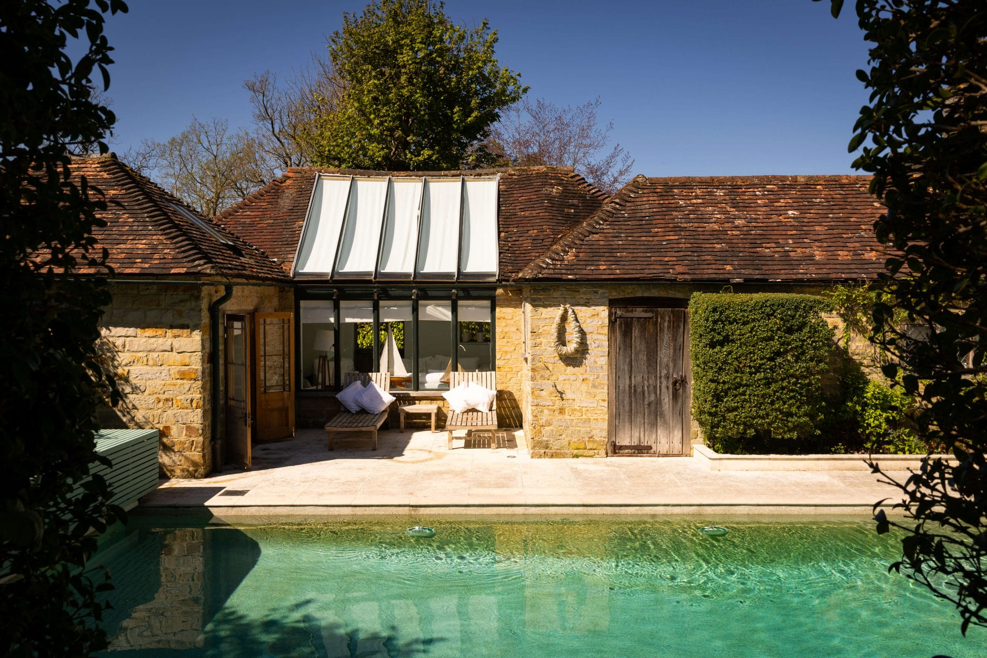a pool house and guest house with wooden sun loungers outside and a large swimming pool, former home of princess margaret