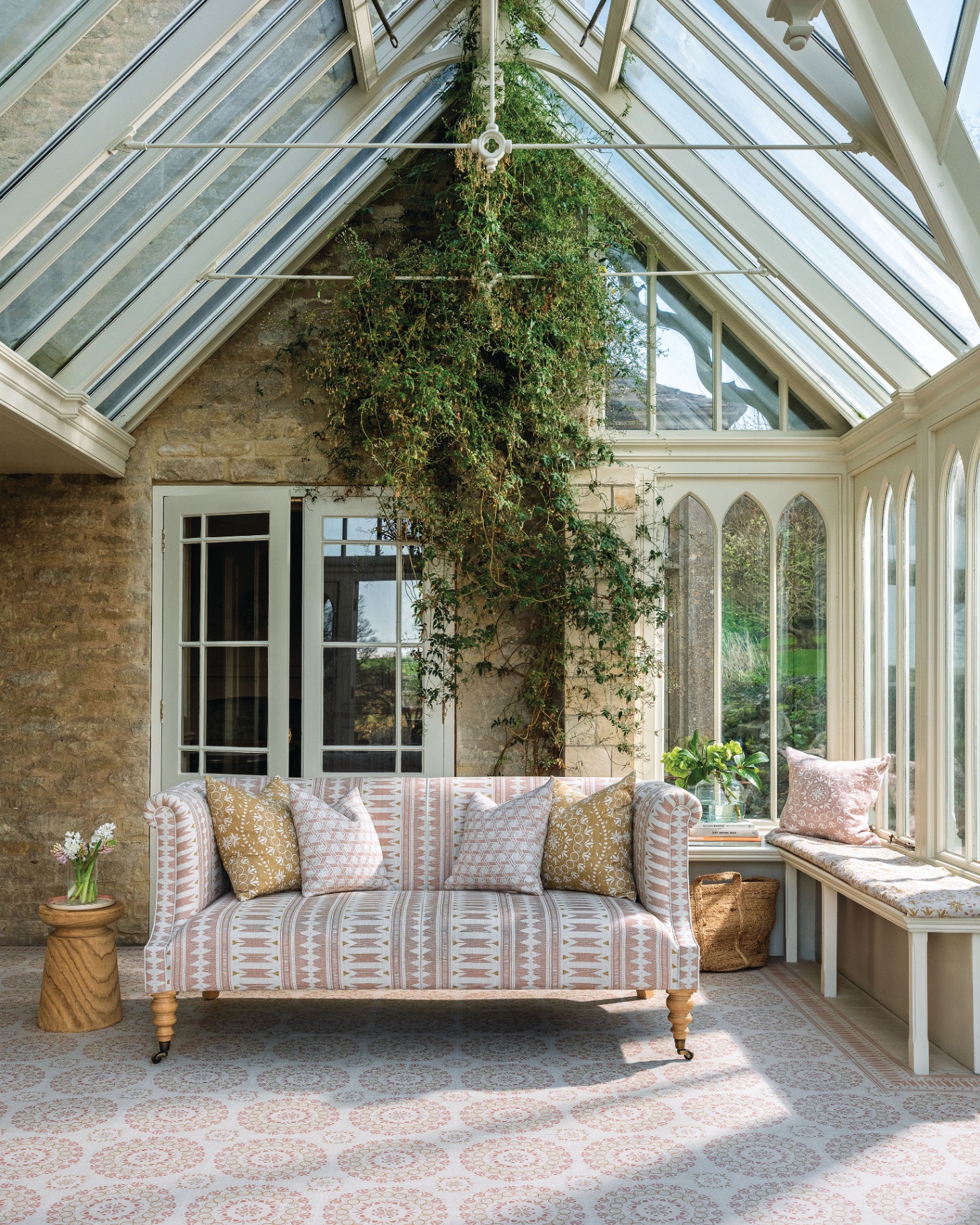 a garden room with trailing greenery that goes up the wall to the ceiling and a patterned sofa with cushions