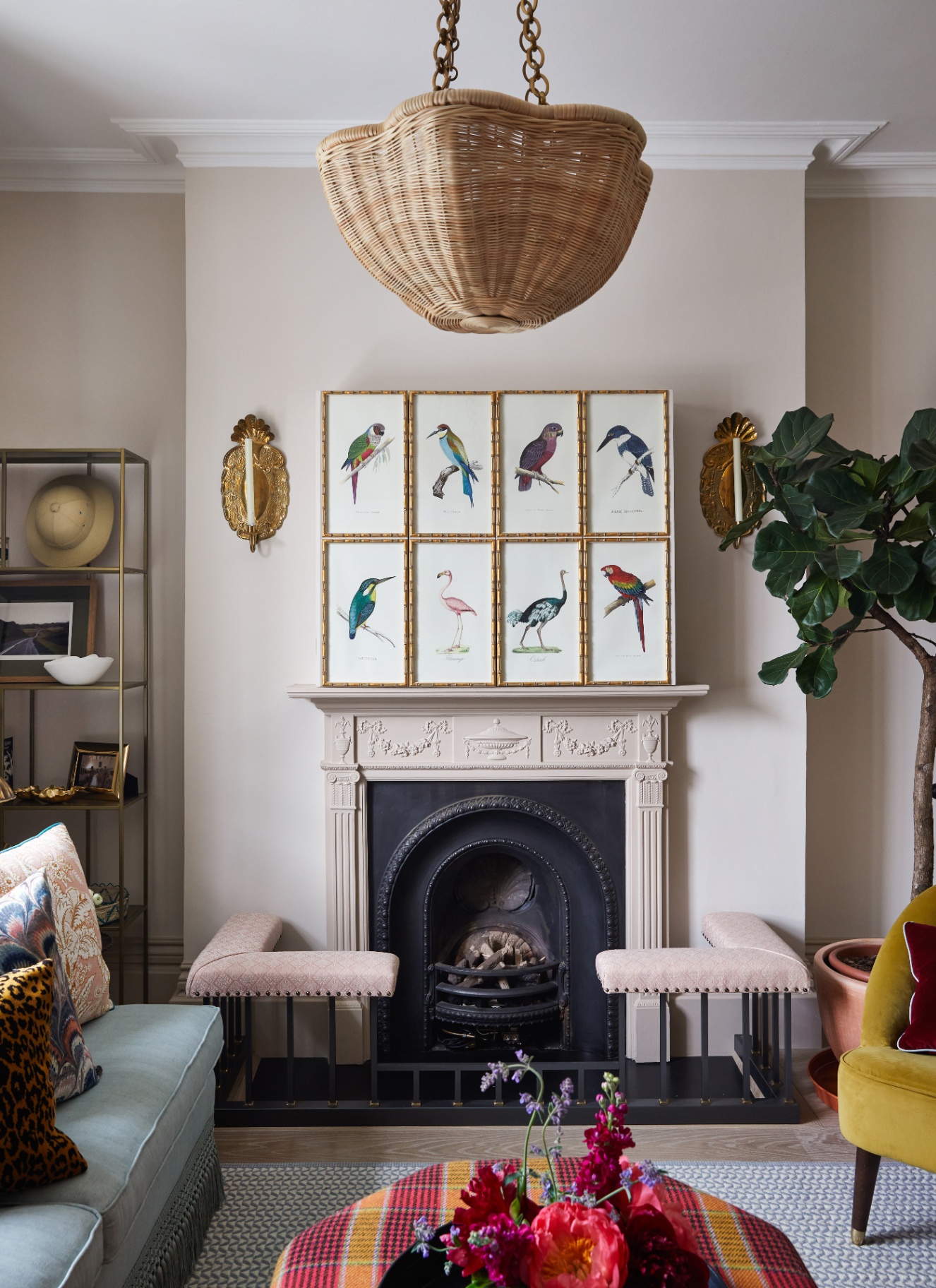 a living room with a large fireplace, a large rattan pendant shade, 8 bird illustrations in gold frames above the fireplace and beige painted walls