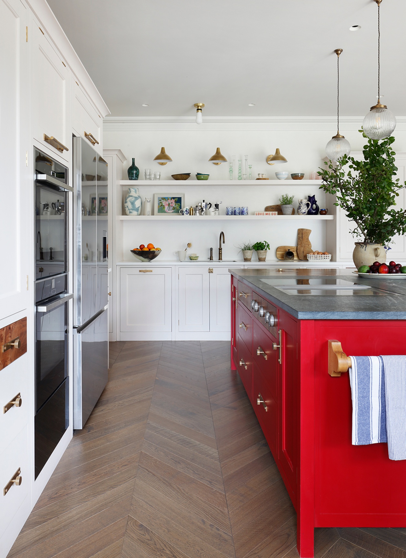 a kitchen with white walls and cabinetry, white long open shelves and a bright red kitchen island